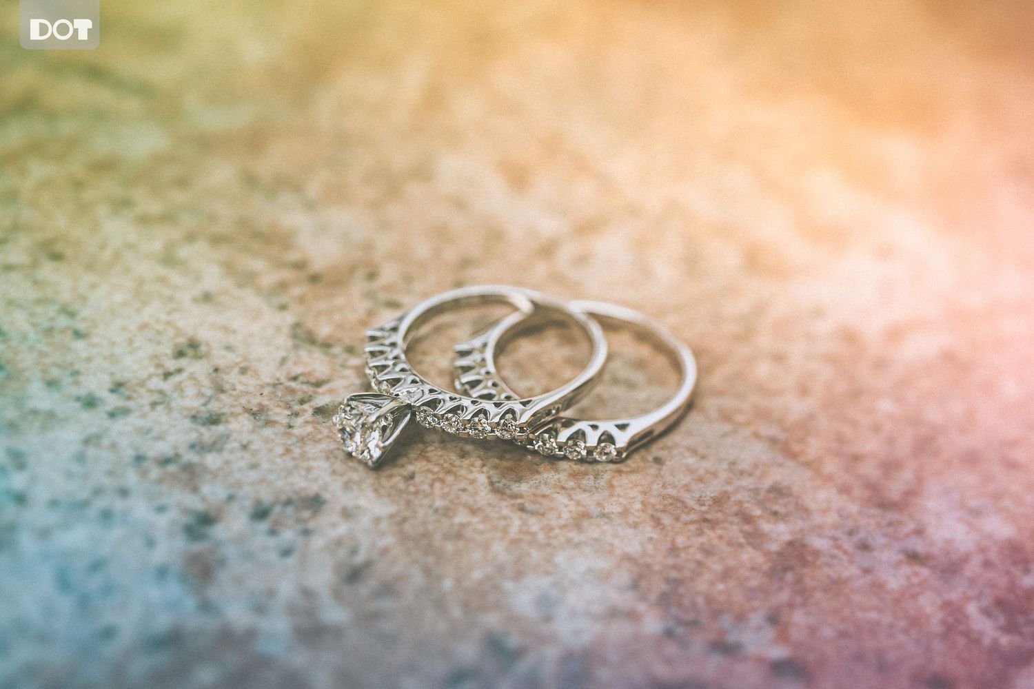 Delicate silver wedding rings with intricate details photographed on a textured surface.