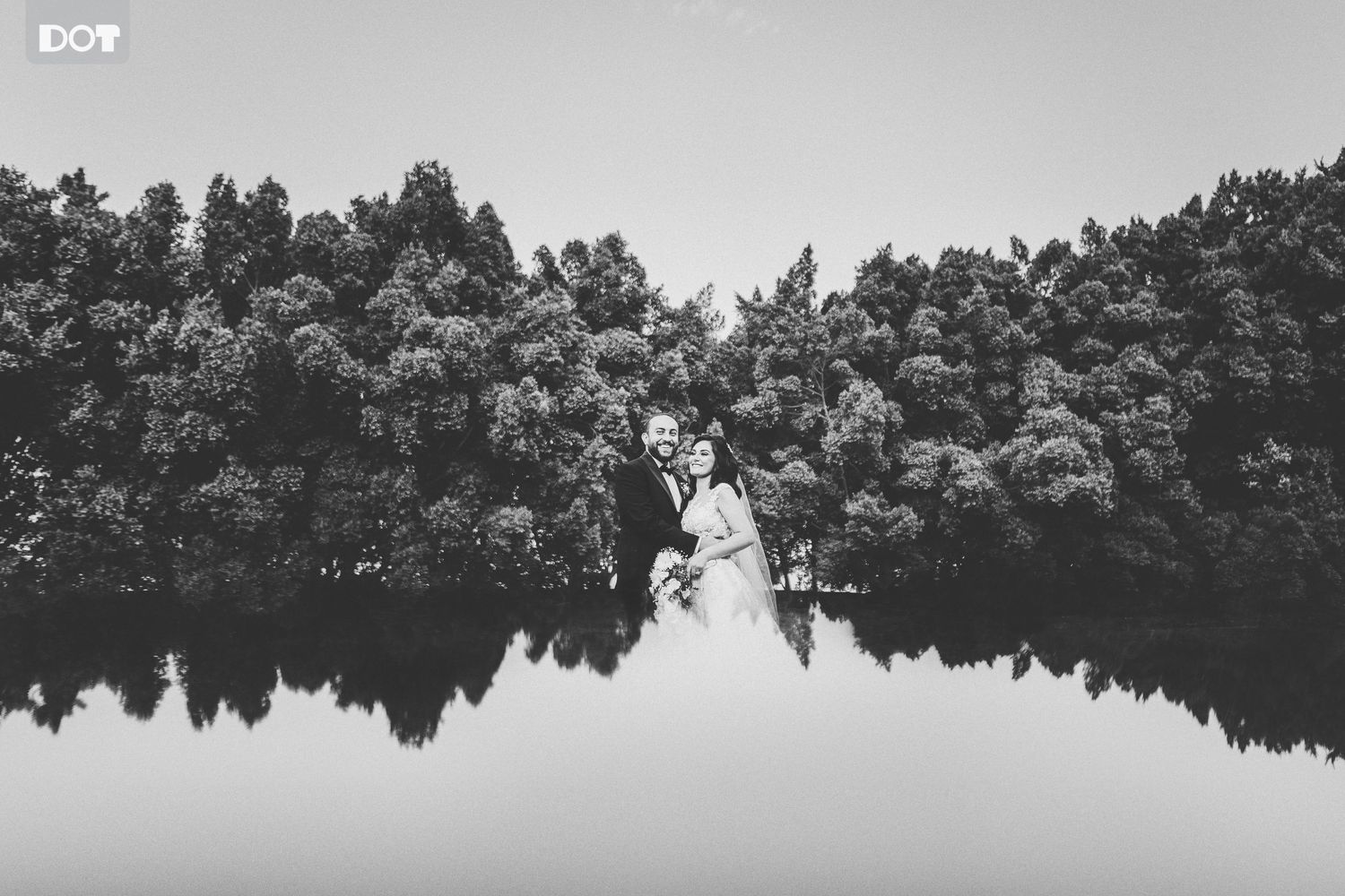 Serene lake landscape with reflections of trees and clouds in black and white.