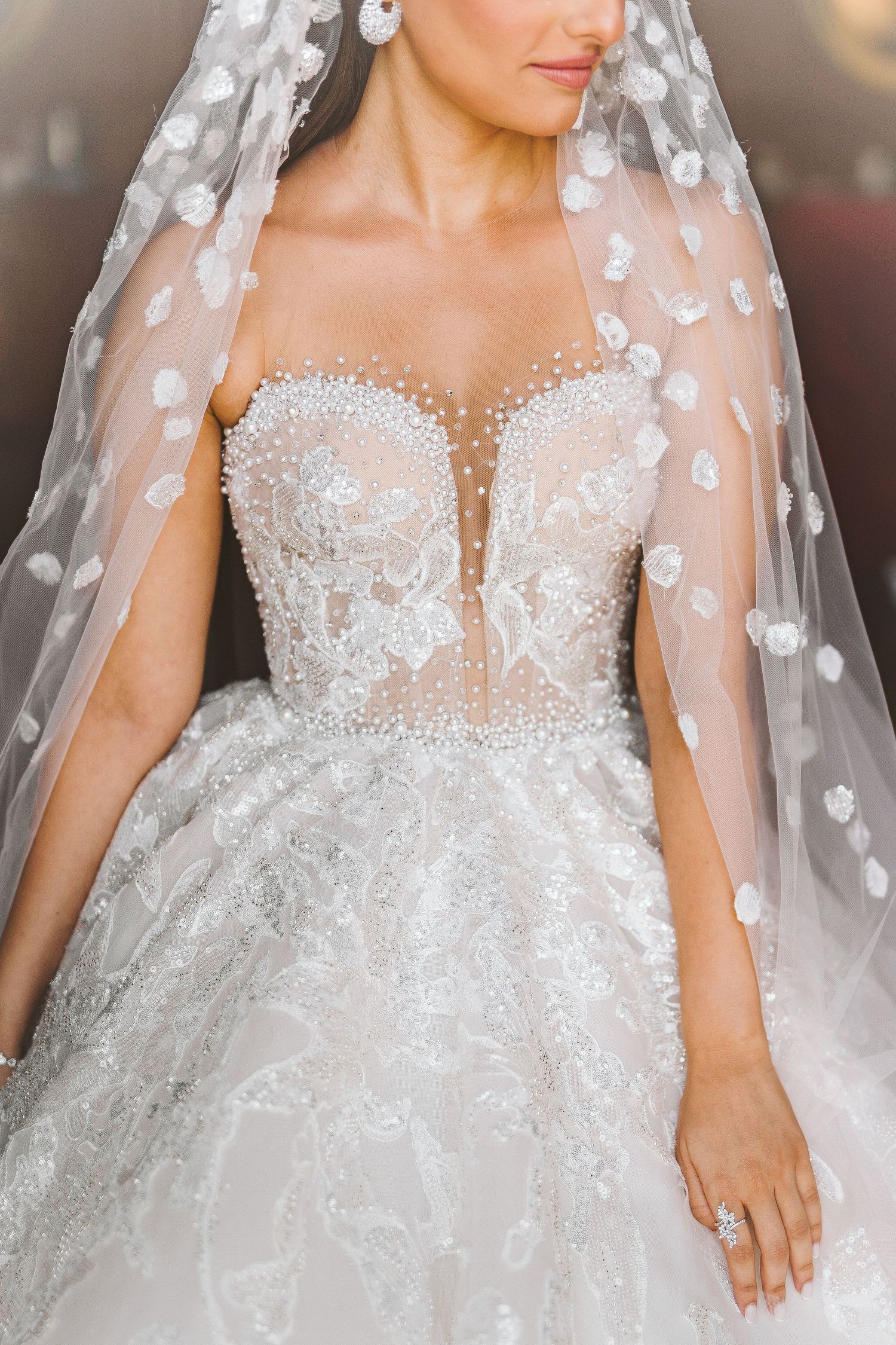 Intricate details of a white wedding dress with delicate lace appliques and sheer fabric overlay.