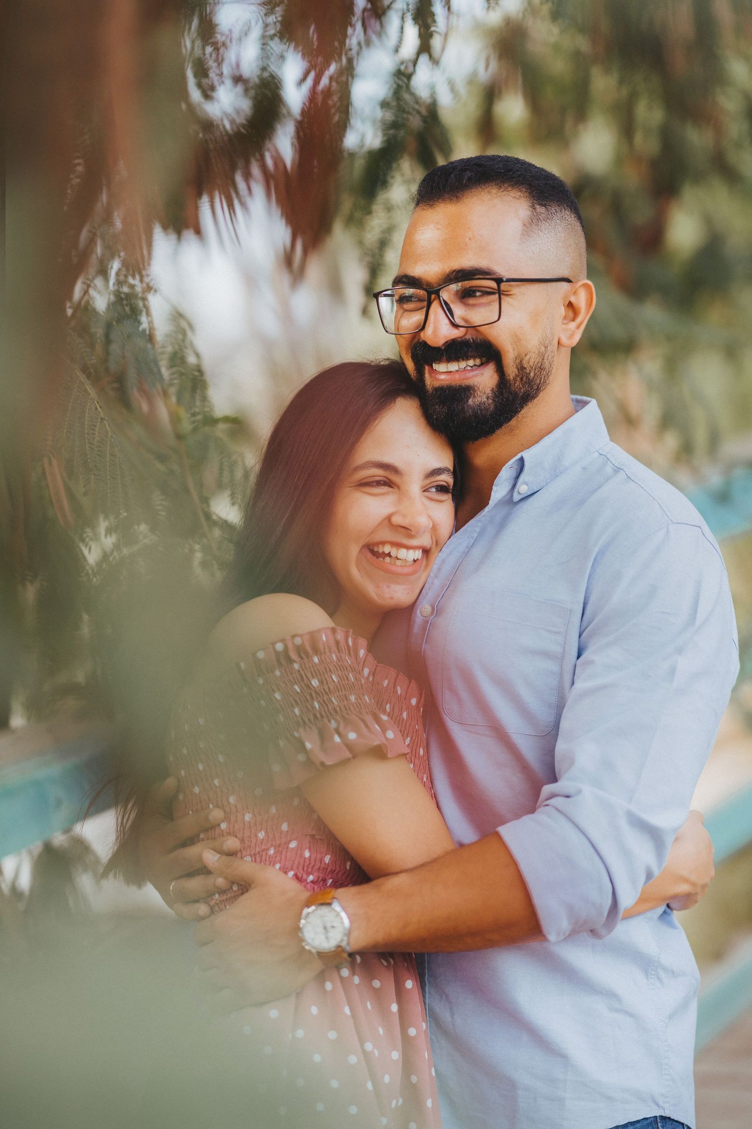 Casual engagement photo session of a couple laughing together under trees.