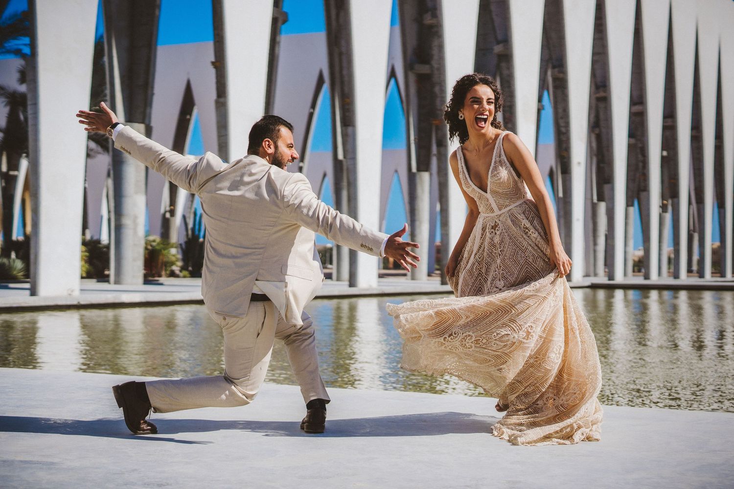 Bride in flowing dress twirling in an outdoor colonnade with repeating white pillars.