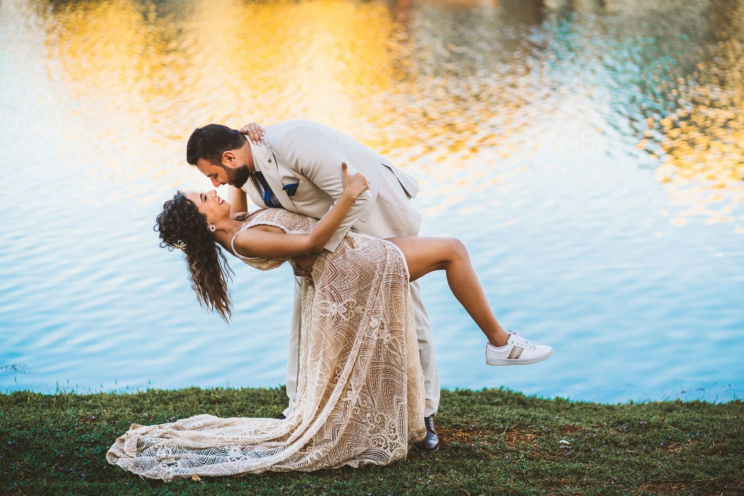 Romantic couple in formal wear poses by a lake at sunset.