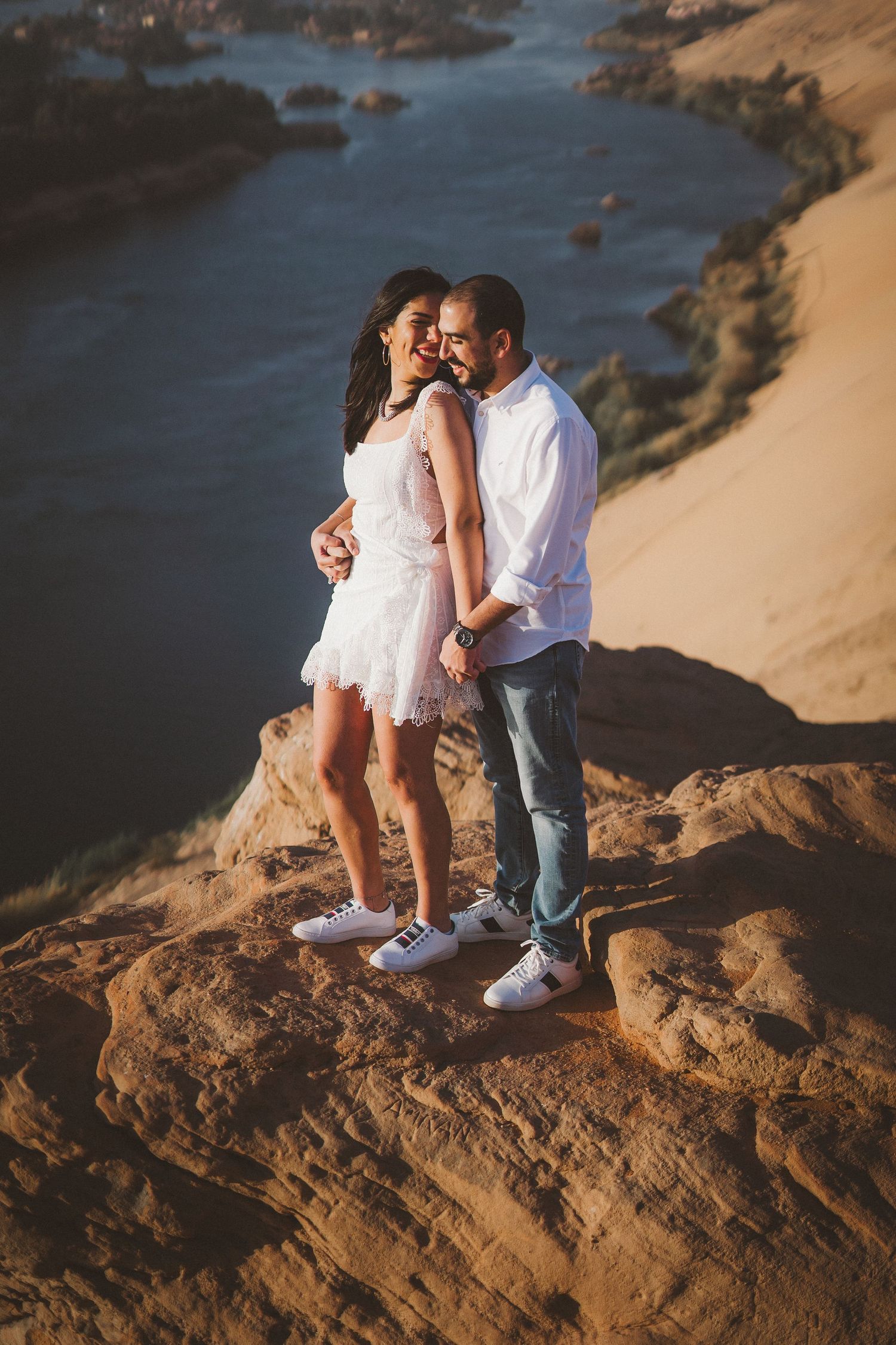 Couple in white clothing shares intimate moments on coastal rocks overlooking the ocean.