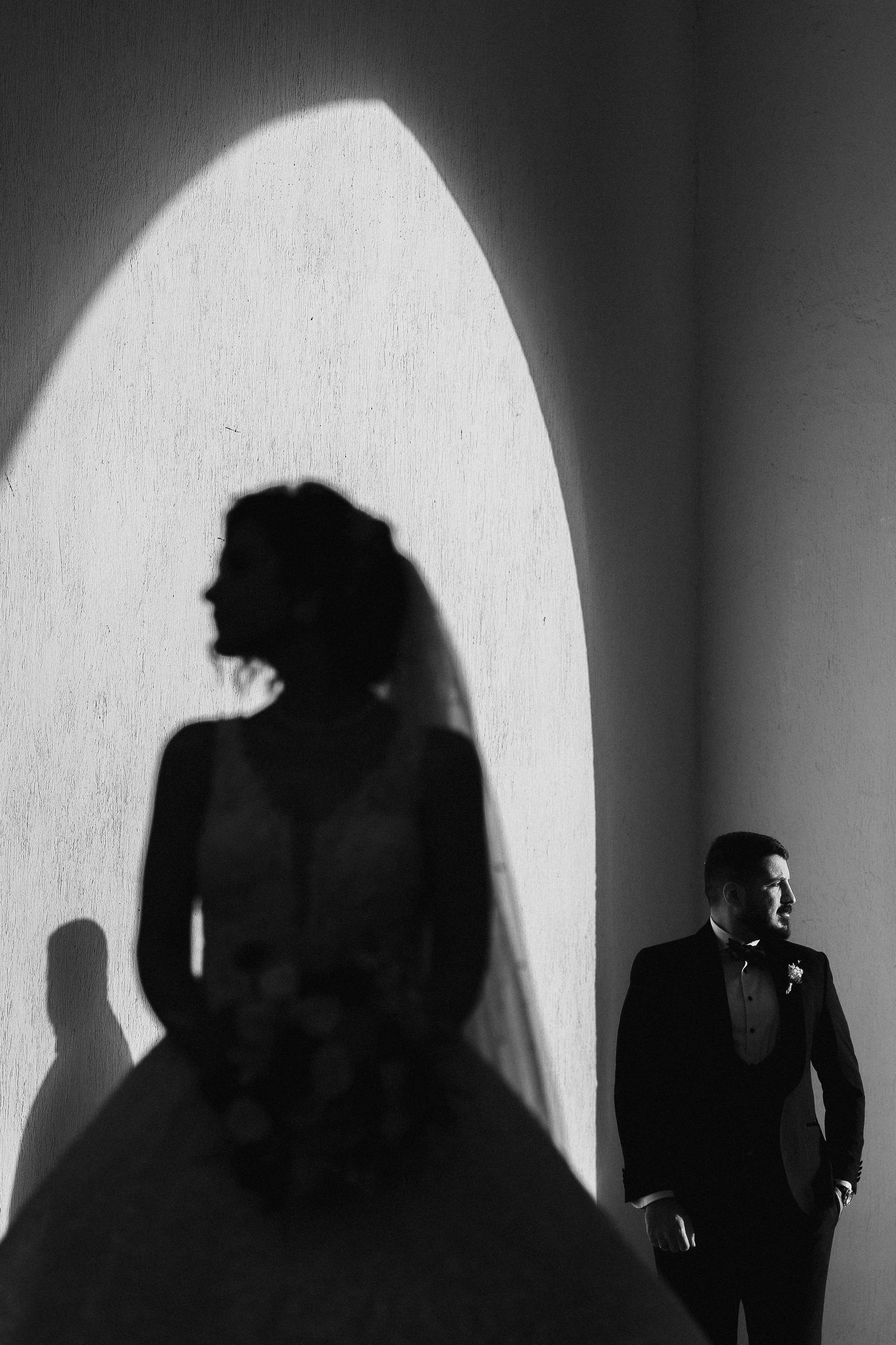 Dramatic black and white wedding photo with silhouette of bride and groom standing in arched doorway.