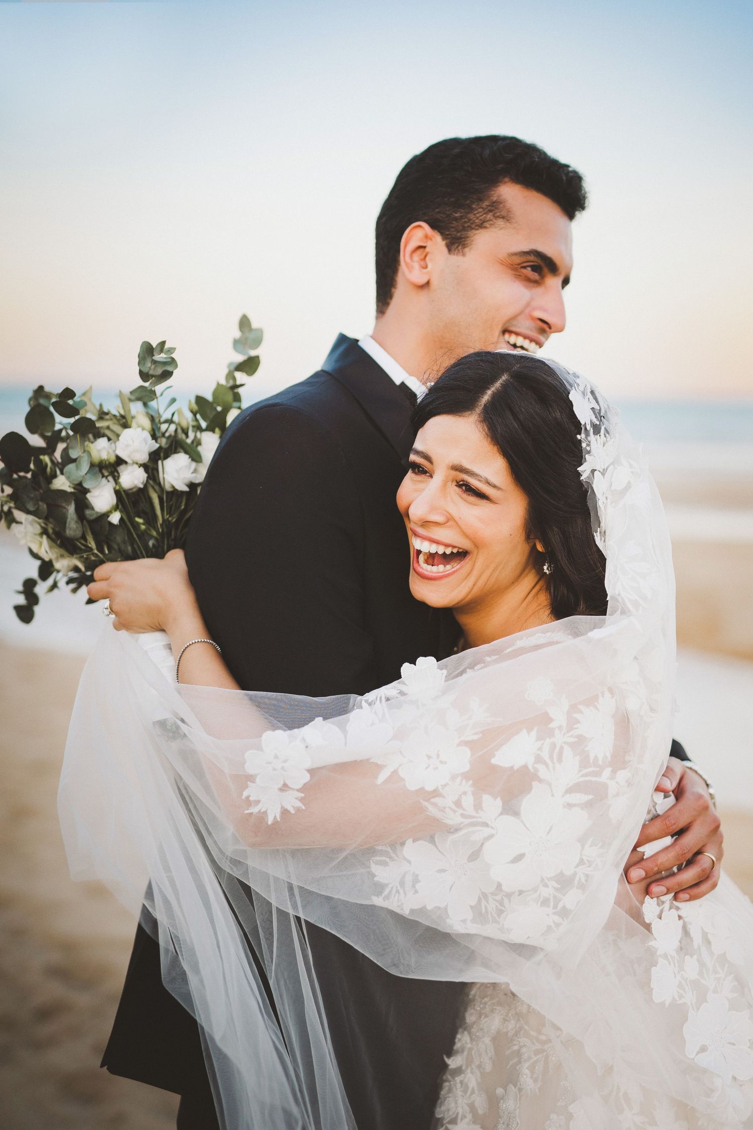 Beach wedding portraits with flowing veil and natural coastal lighting.
