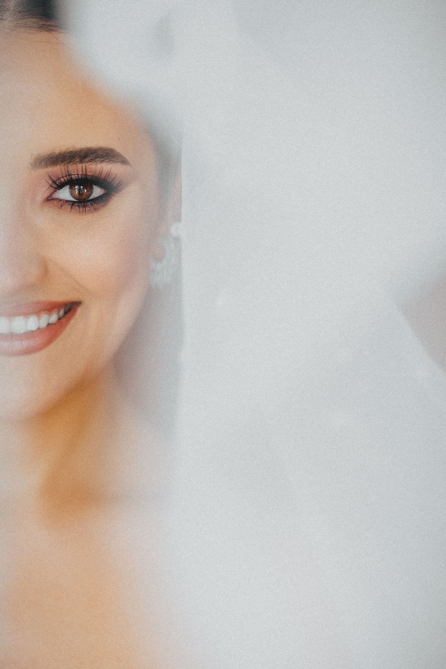 Close up portrait showing half of bride's face with soft smile and eye makeup.