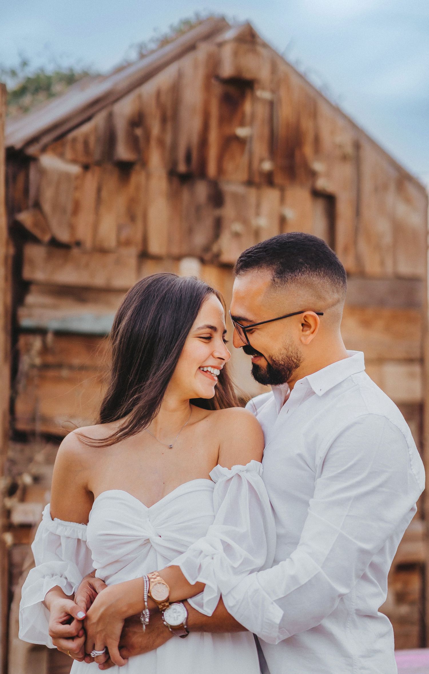 Intimate engagement photo of couple sharing tender moment near rustic wooden building.