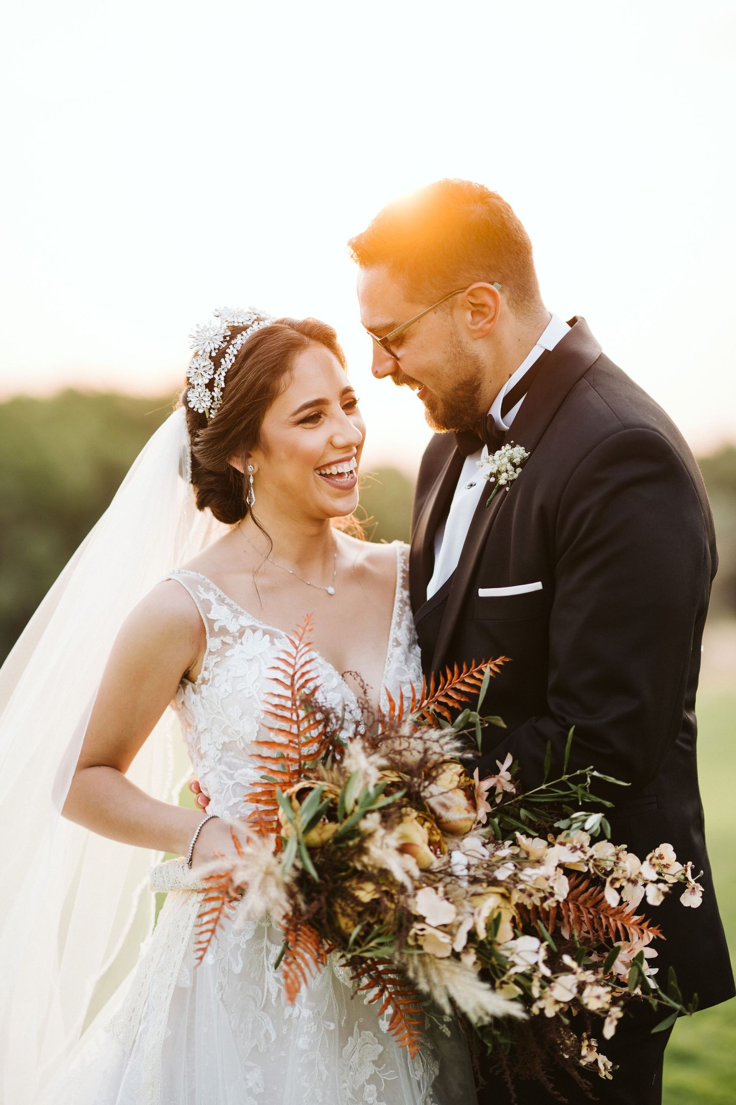 Candid wedding portrait of couple laughing together with autumn-toned bouquet at sunset.
