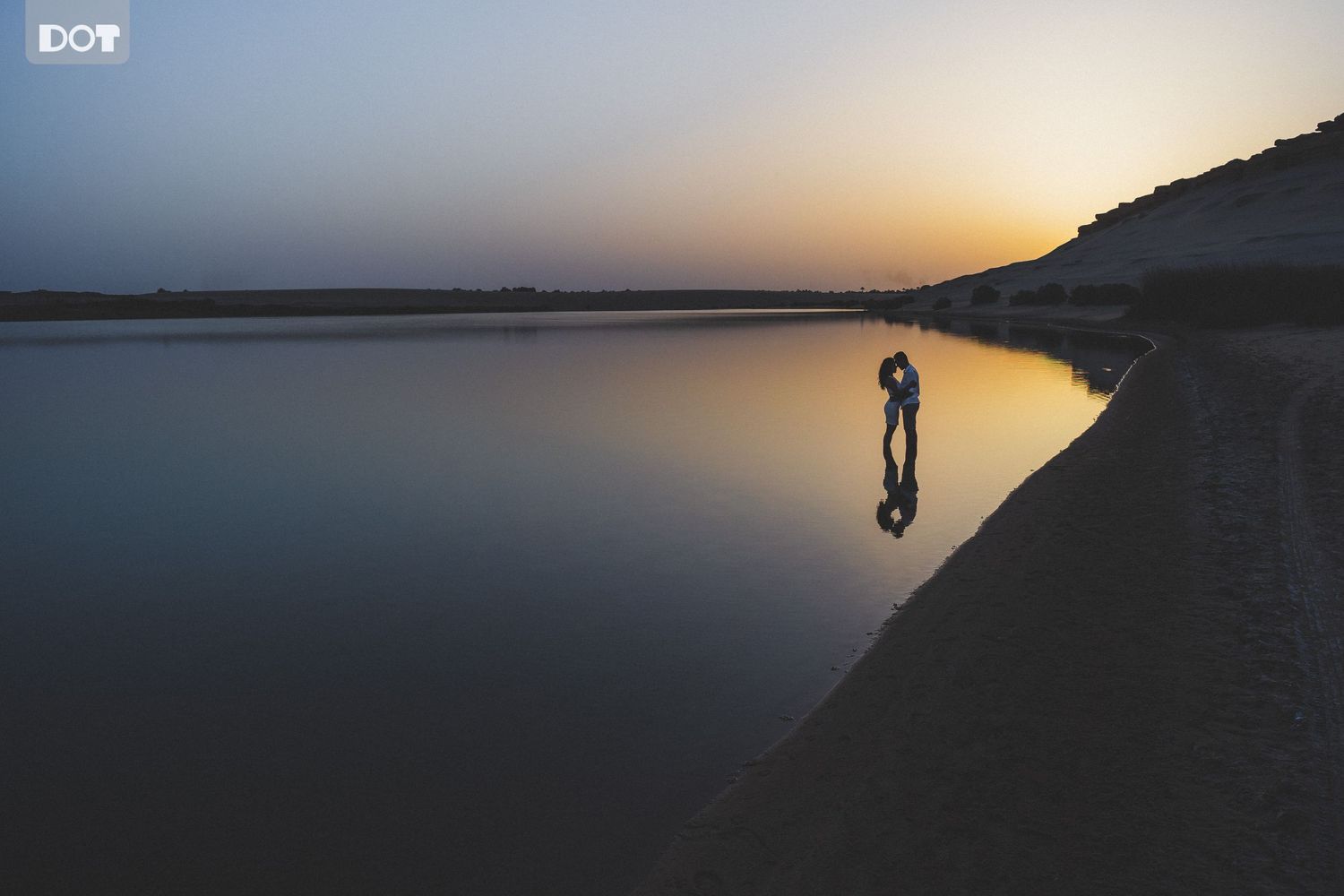 A silhouette of a figure reflected in still water at sunset.
