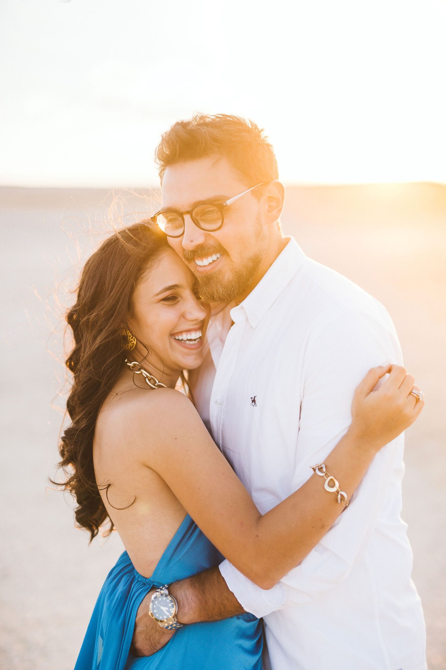A sunset portrait of a laughing couple in casual attire on the beach.
