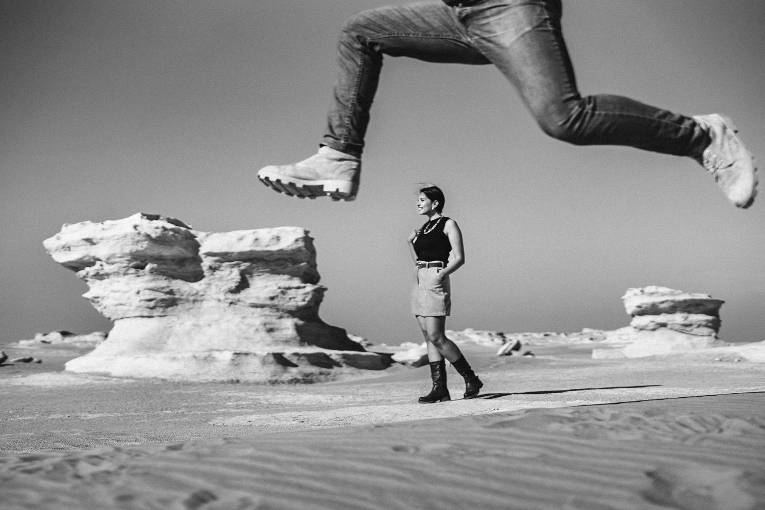 A creative desert photo with someone jumping over a person standing near rock formations.