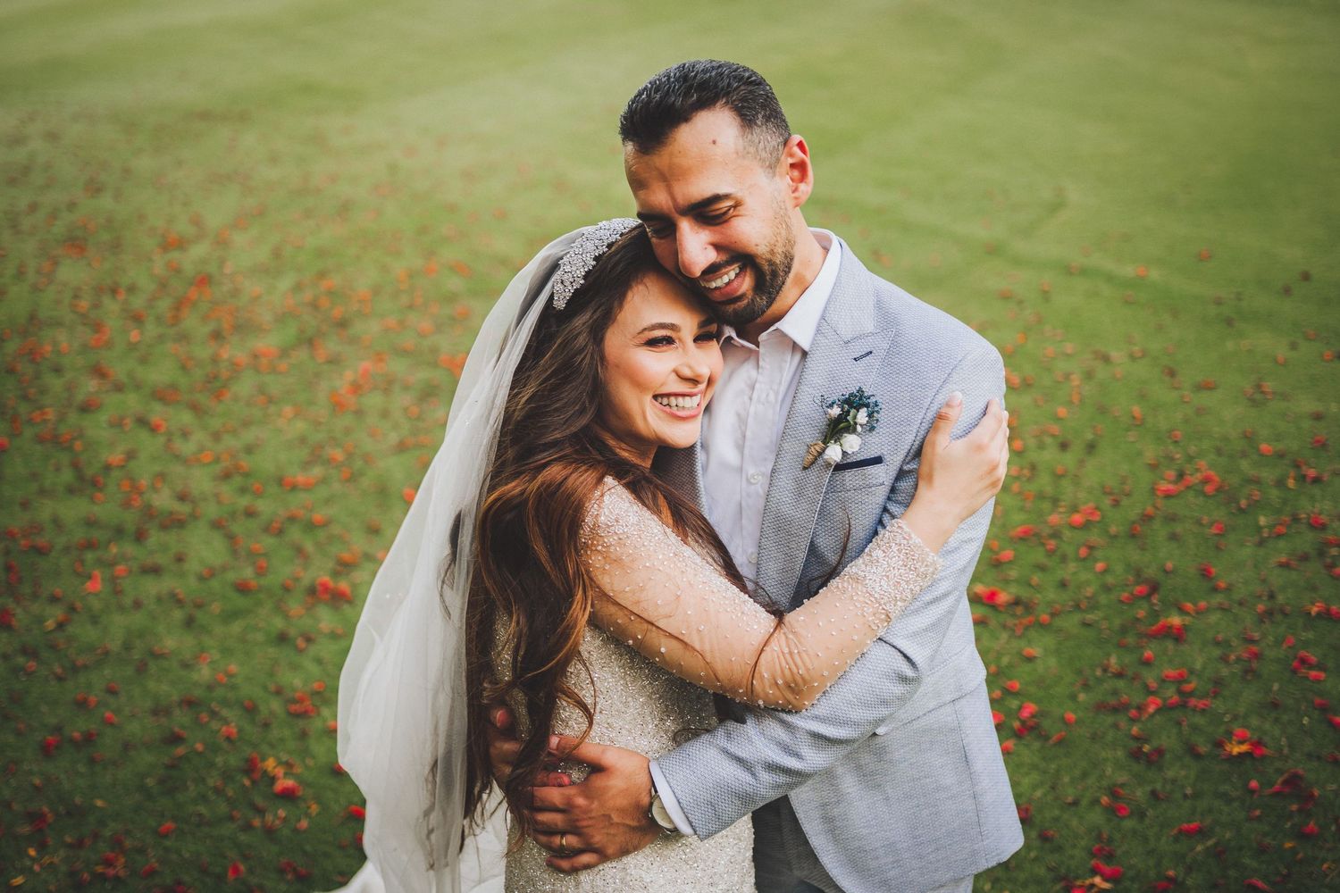 Joyful wedding couple embracing on grassy lawn with bride in flowing veil.