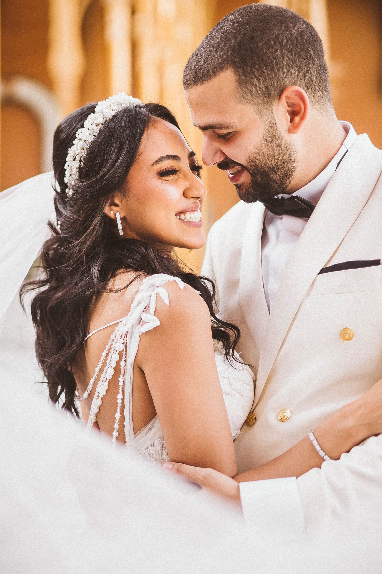 Intimate moment between newlyweds in white formal attire with crystal headpiece detail.