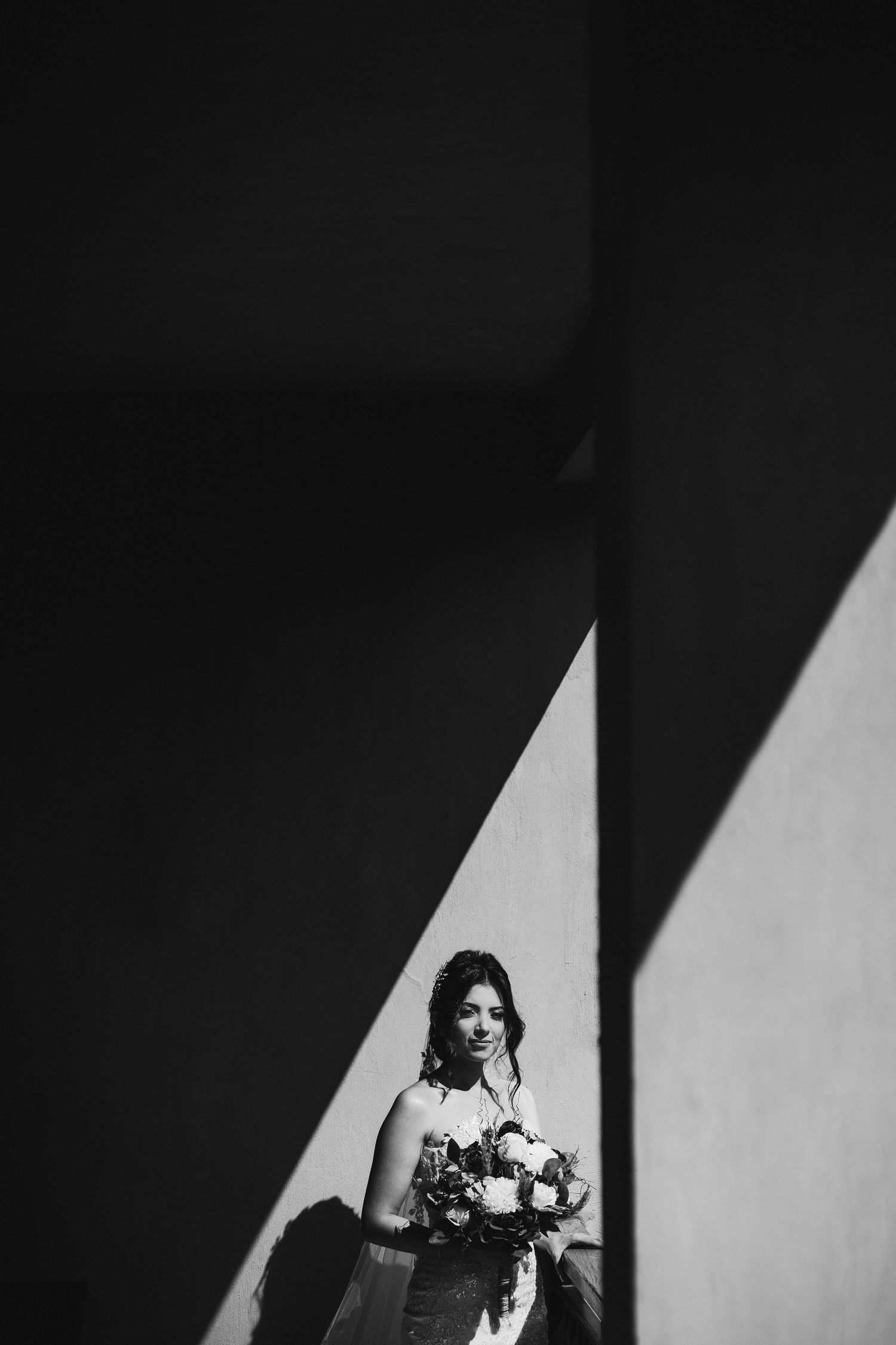 Artistic black and white bridal portrait framed by dramatic architectural shadows.