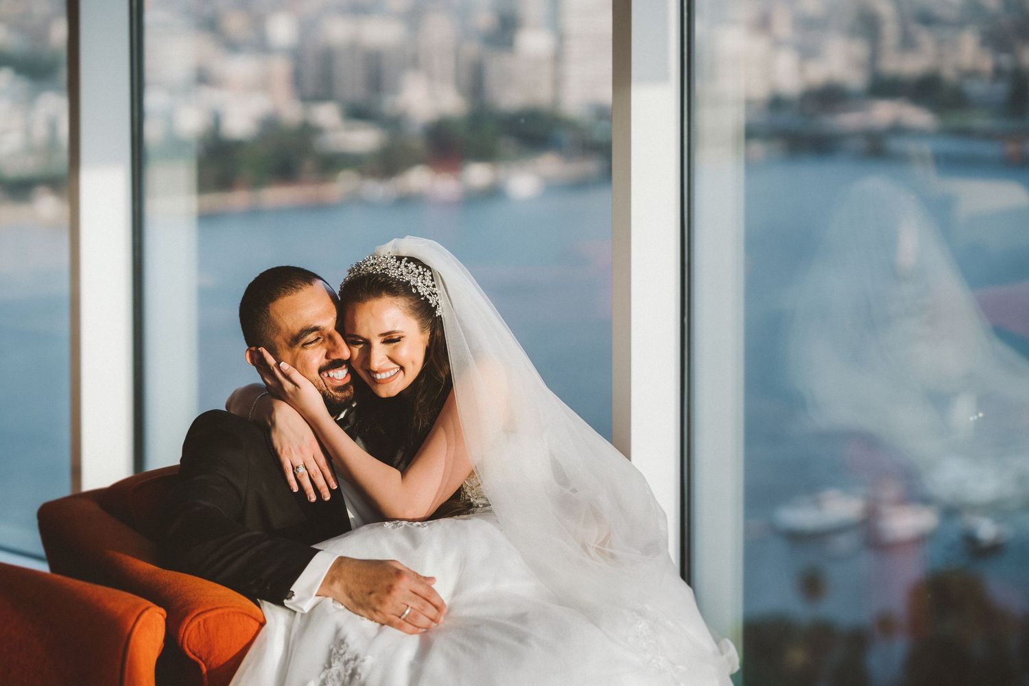 Couple sharing tender moment on high-rise balcony overlooking waterfront cityscape.