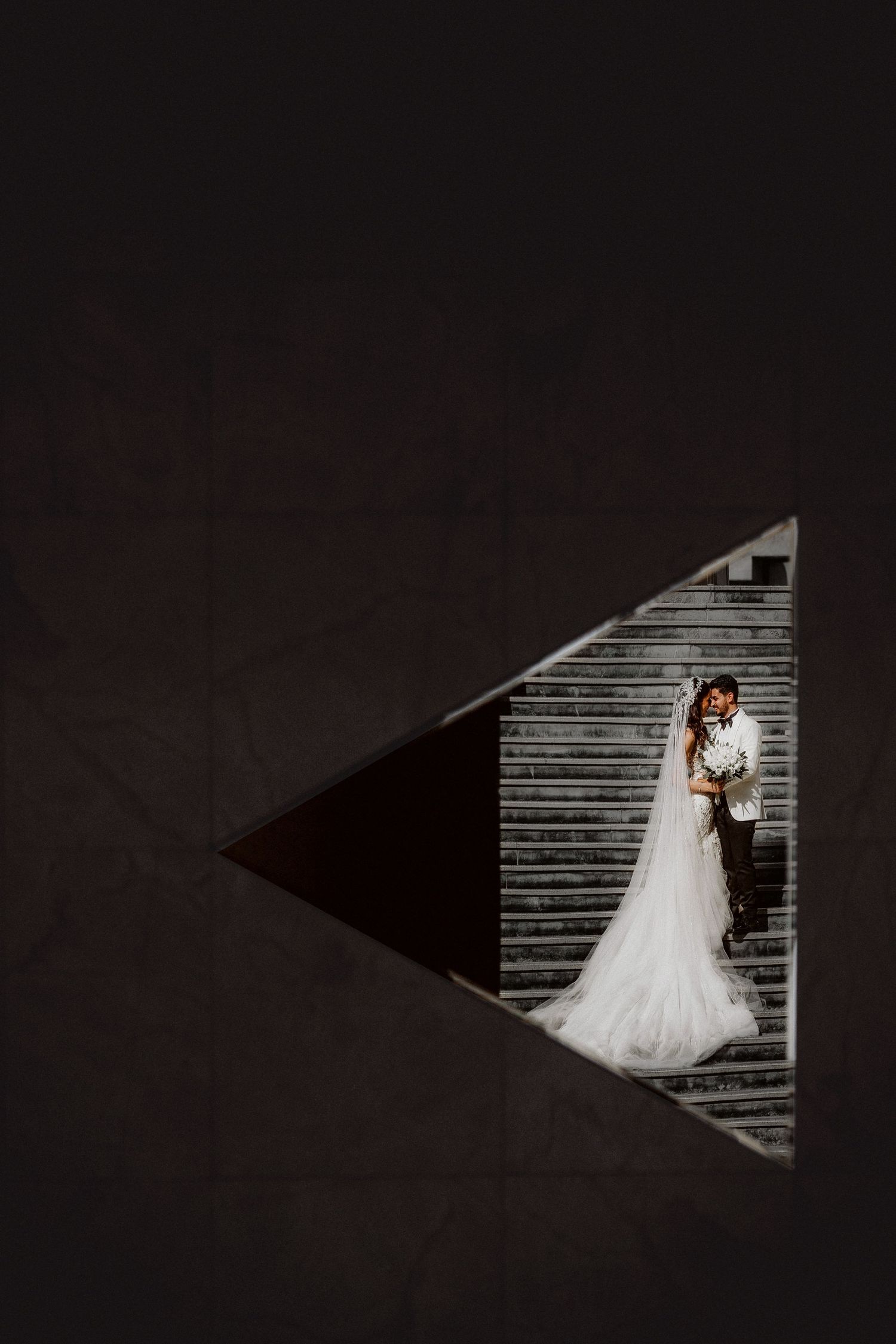 A dramatic triangular composition shows a bride against a wooden wall in black and white.