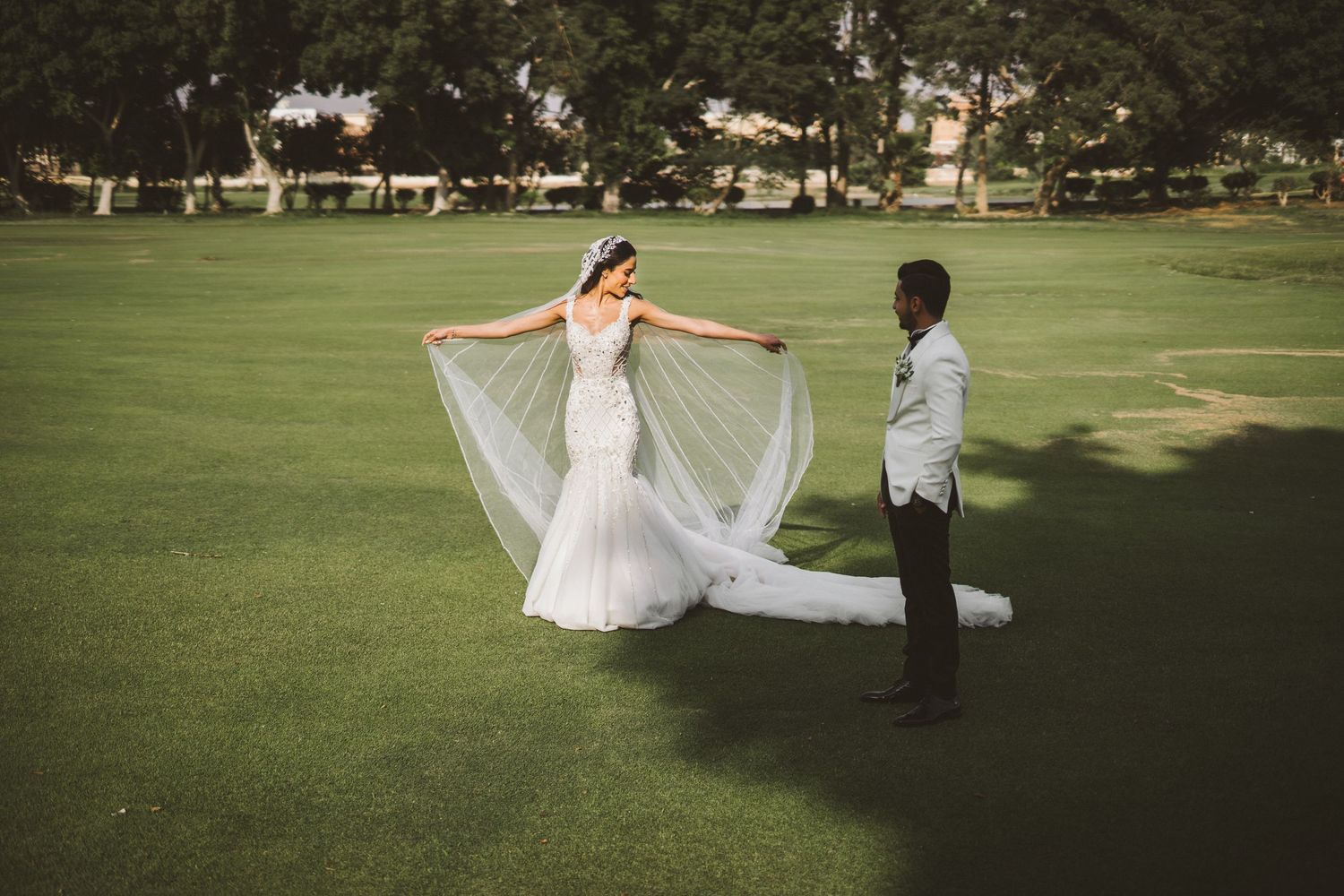 A couple dances on a green lawn with the bride's veil flowing in the breeze.