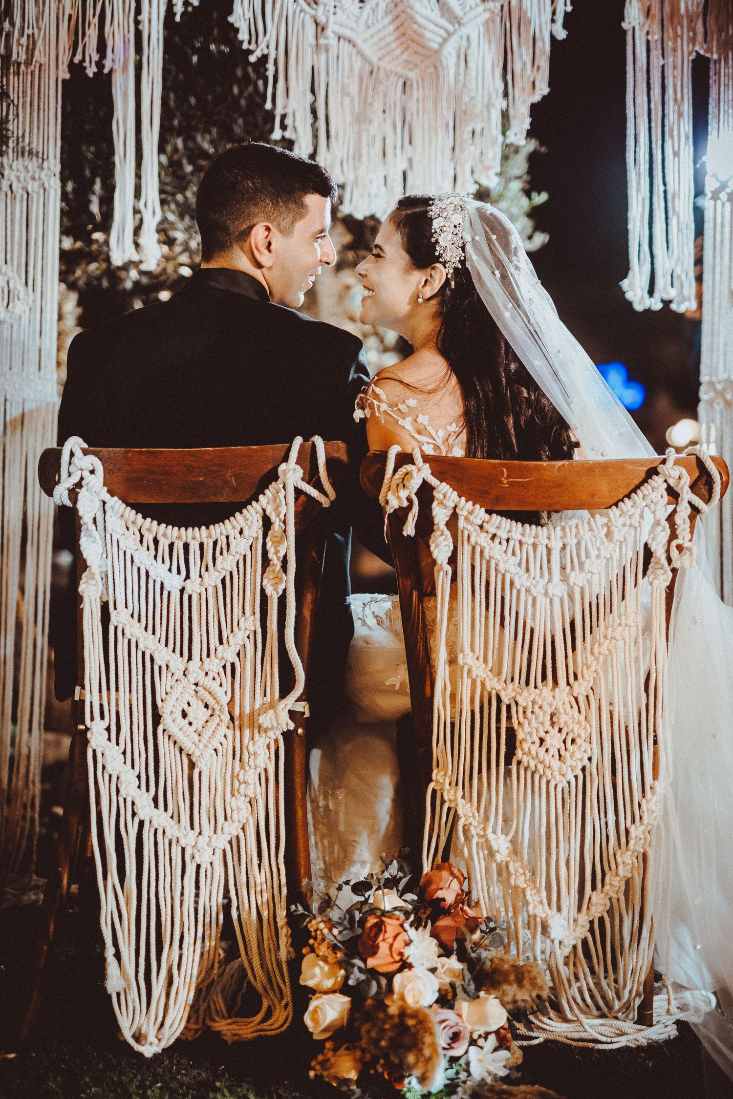 Newlyweds sitting in decorated macrame chairs sharing an intimate moment.