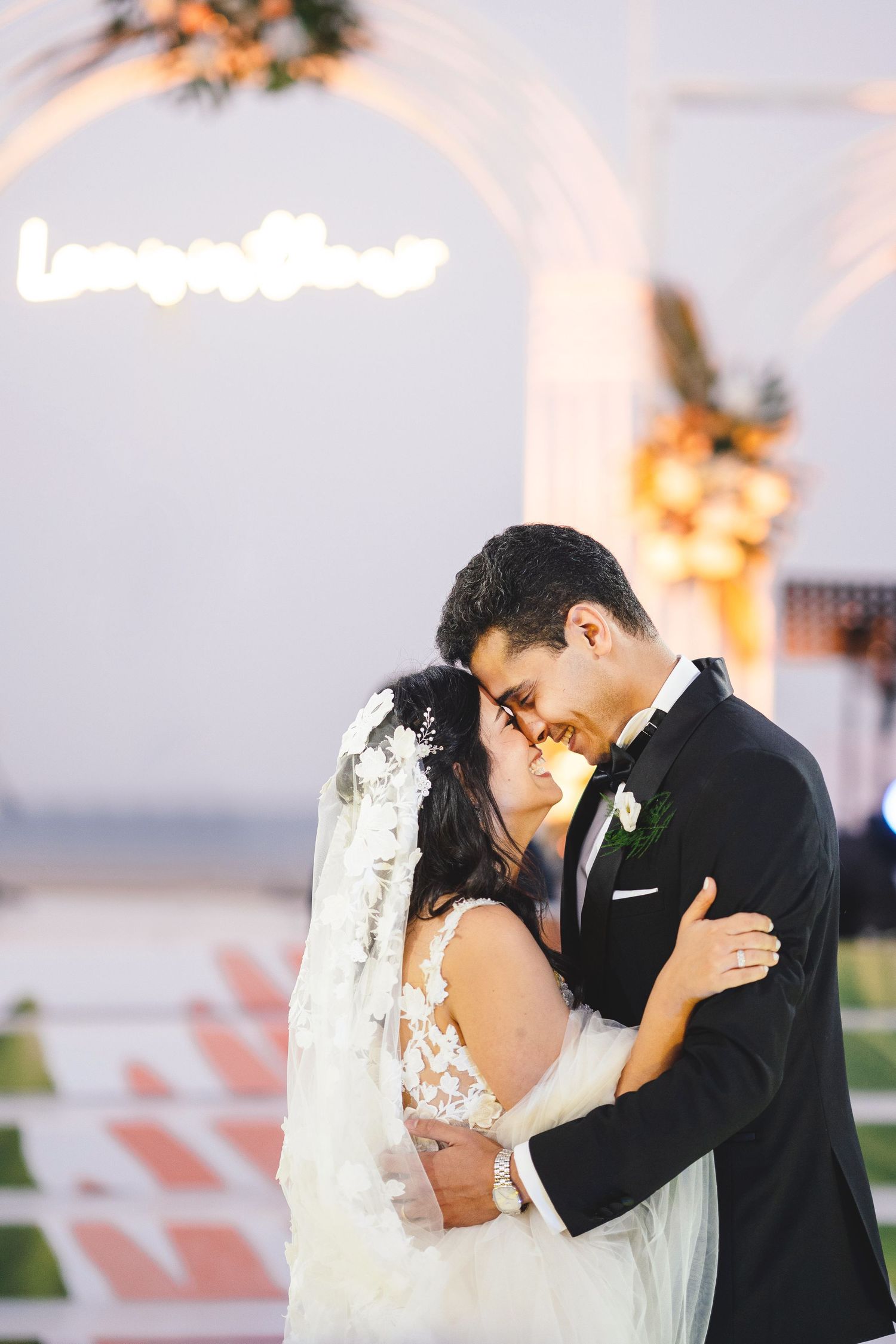 Intimate wedding moment under a neon 'together' sign with floral decorations.