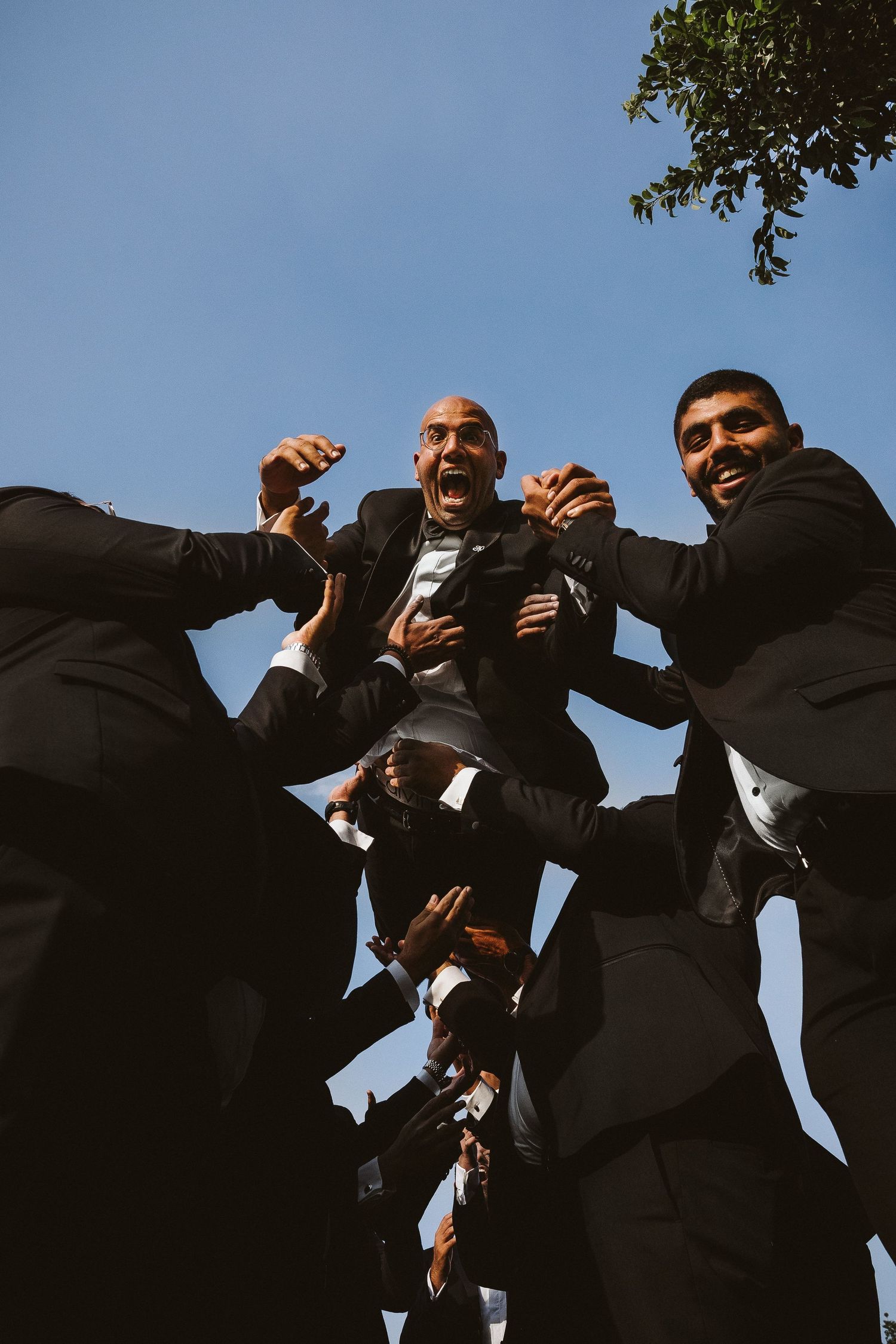 Low angle shot of groomsmen in black suits against blue sky.