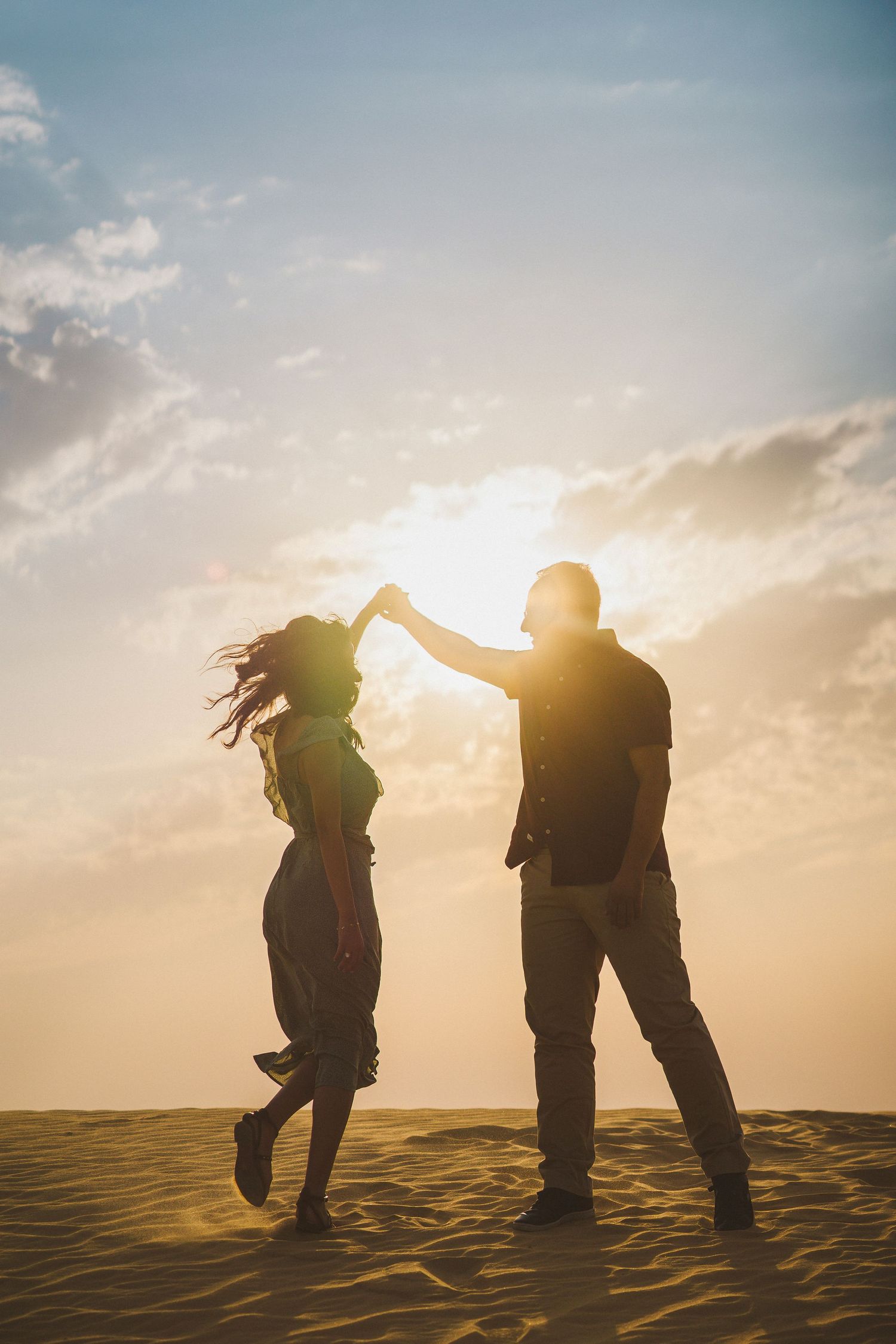 Silhouettes of people playfully posing against a dramatic sunset on sand dunes.