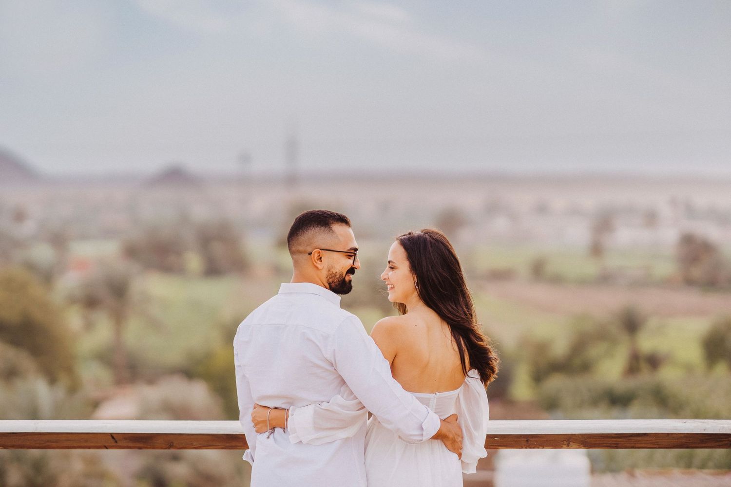 Couple embracing while looking out at a desert landscape during golden hour.