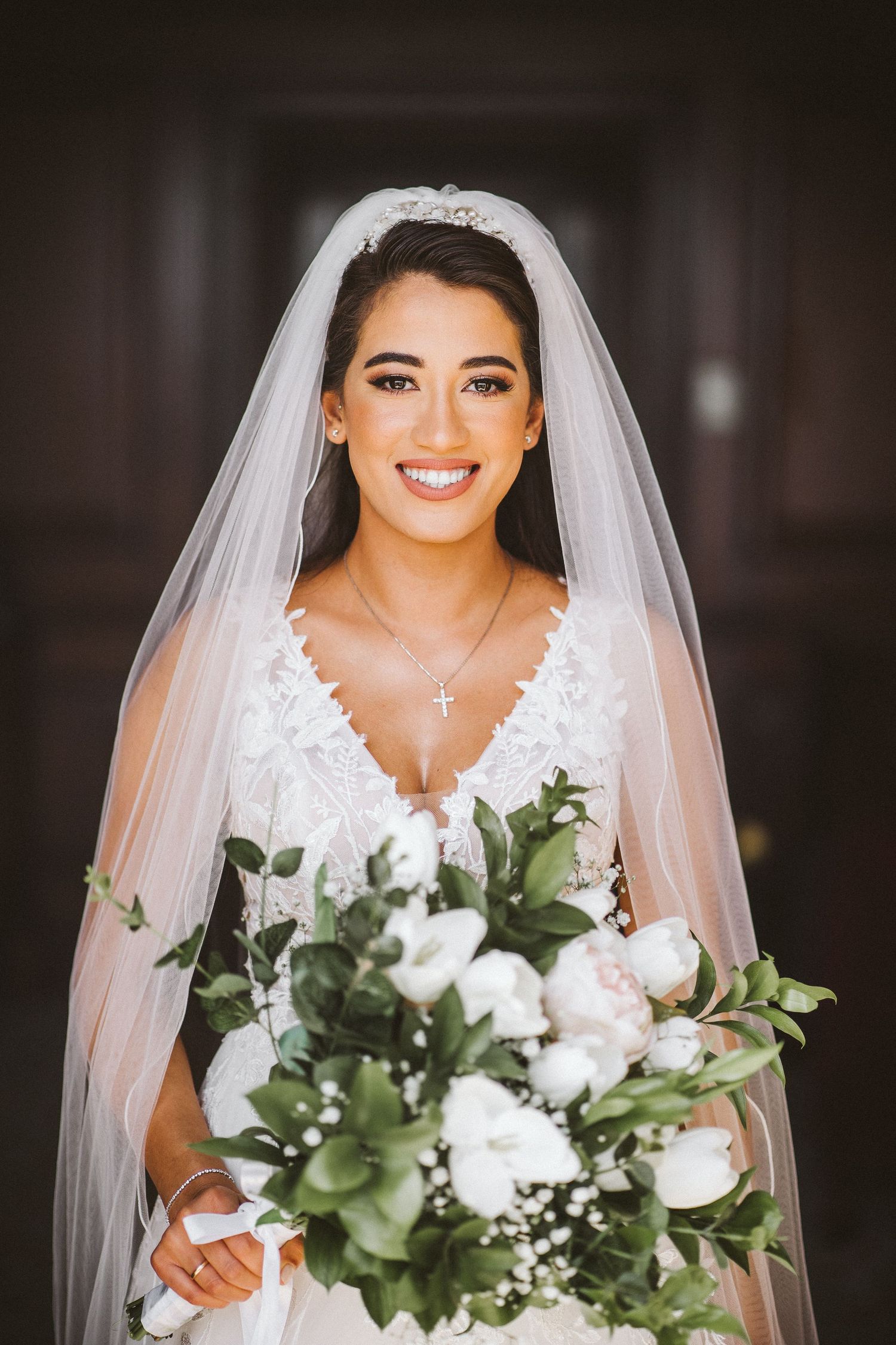 Elegant bridal portrait showcasing a white floral bouquet and lace wedding dress with veil.