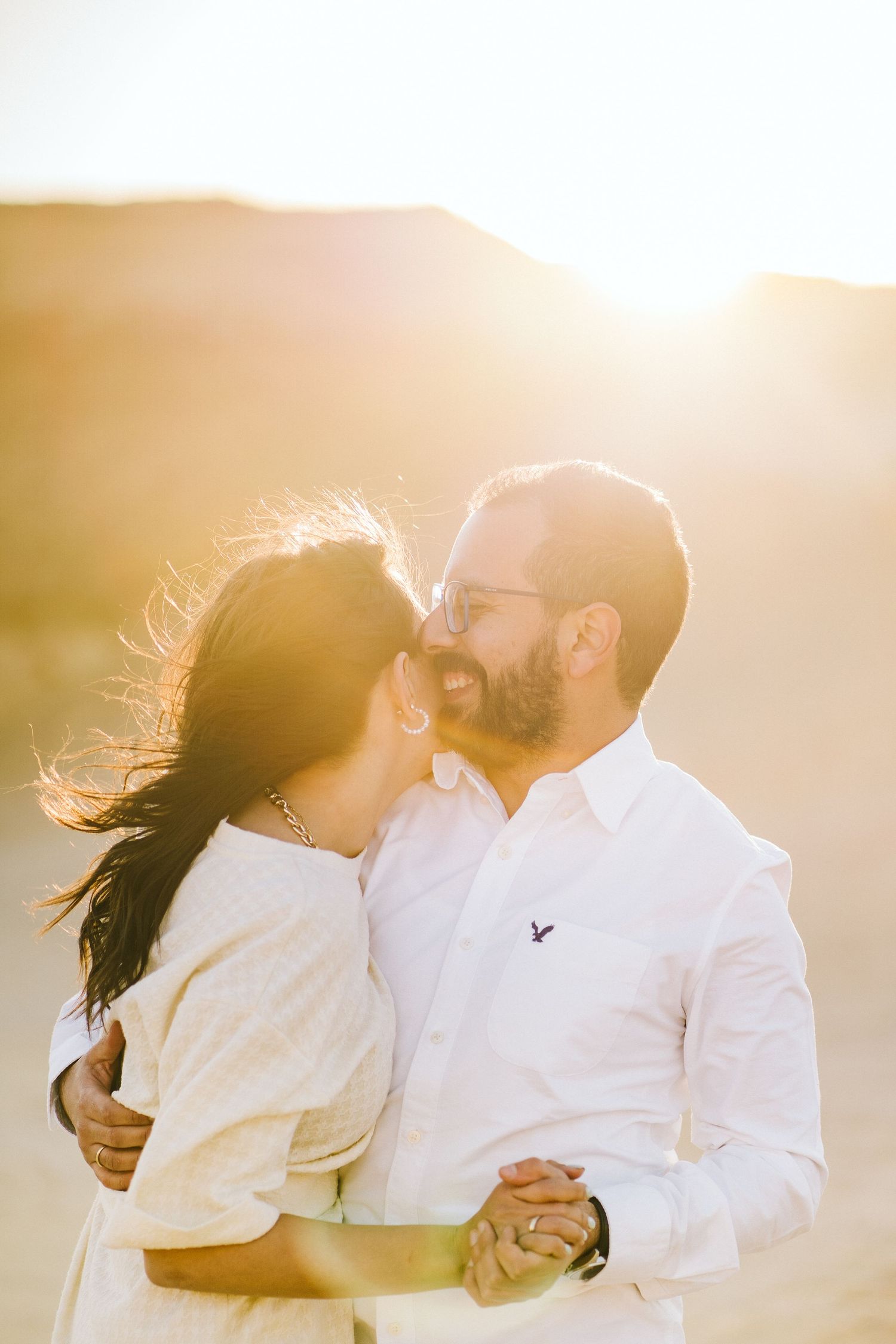 Romantic couple in white outfits embracing during golden hour photoshoot.