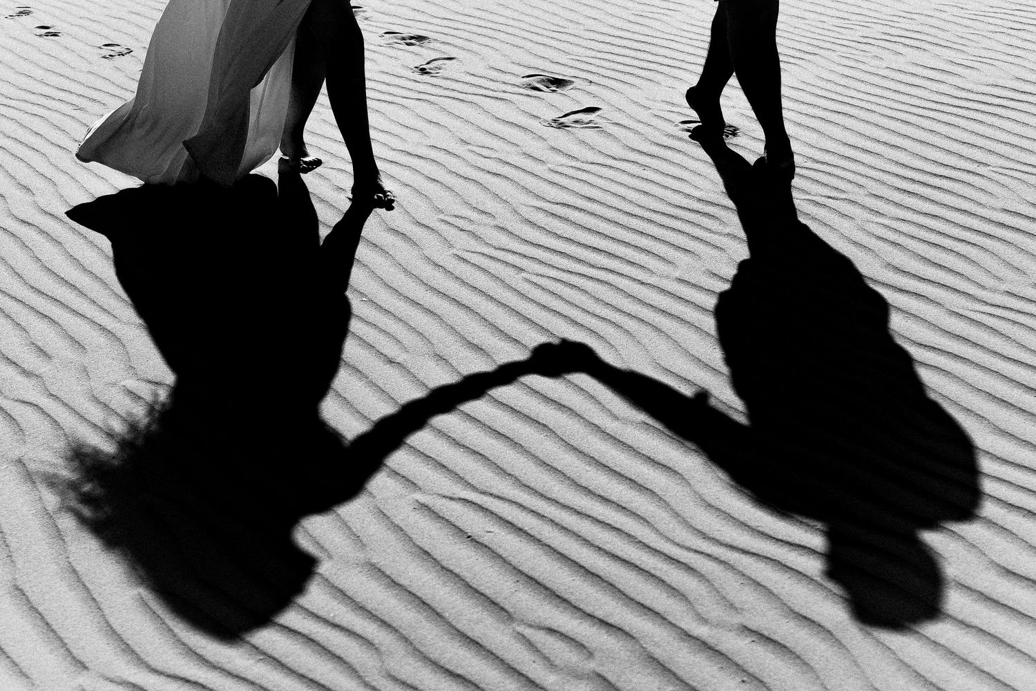 Black and white silhouettes of people dancing on textured sand.