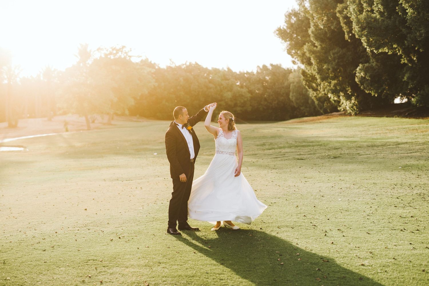 Wedding couple walking through a sunlit field during golden hour.