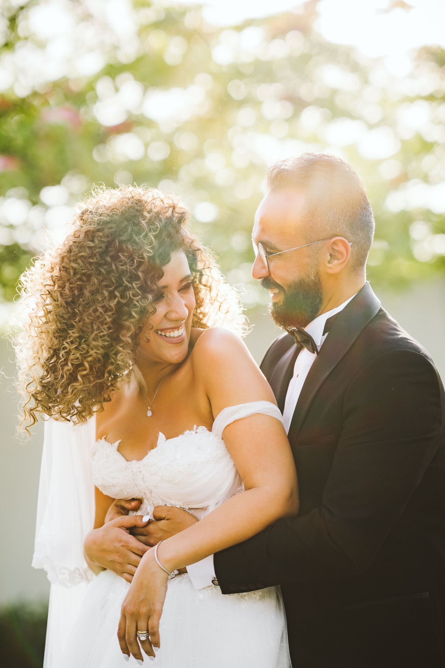 A joyful wedding couple shares an intimate moment in golden sunlight with the bride wearing a strapless gown.