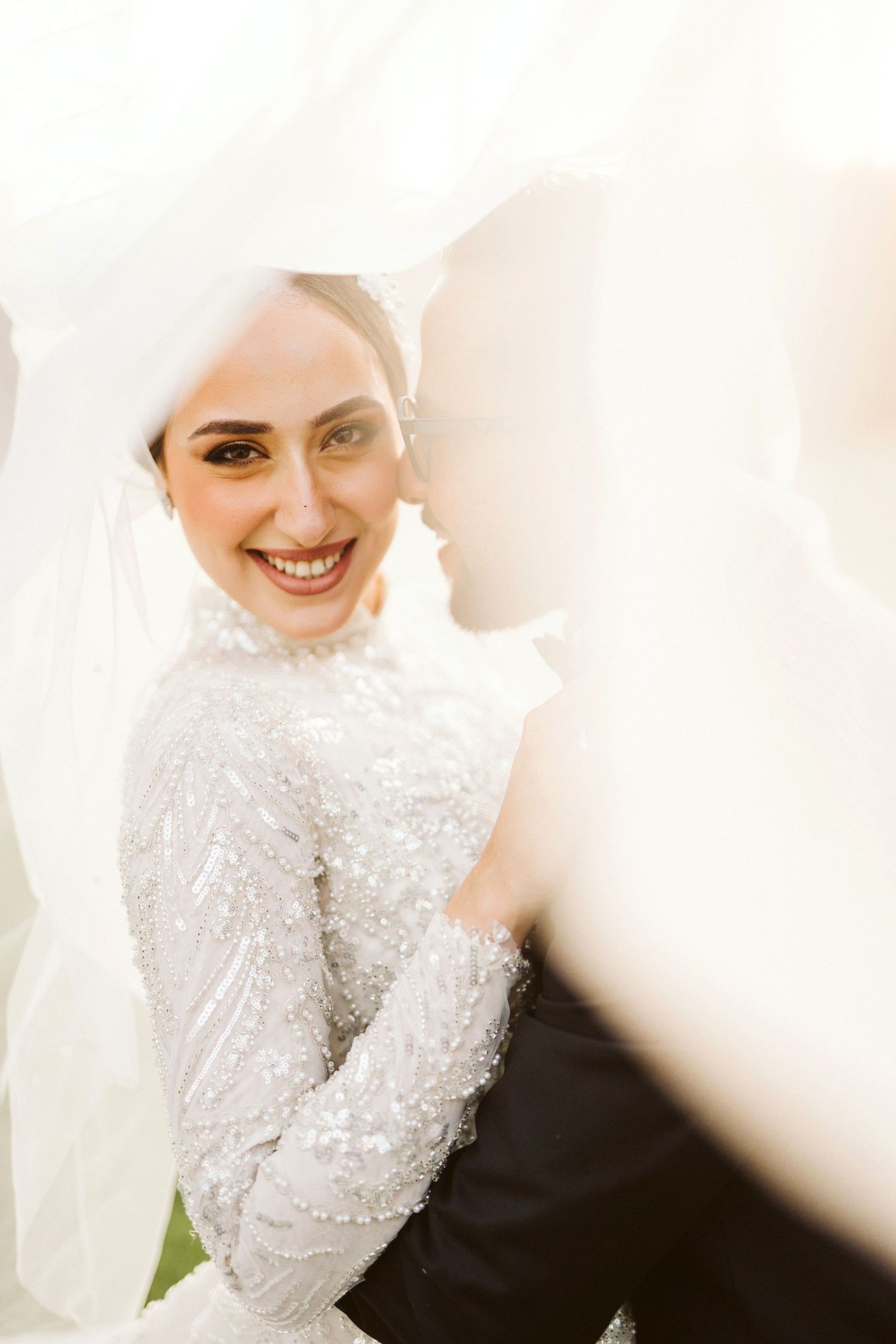 Intimate wedding portrait with bride in long-sleeve lace gown and flowing veil.