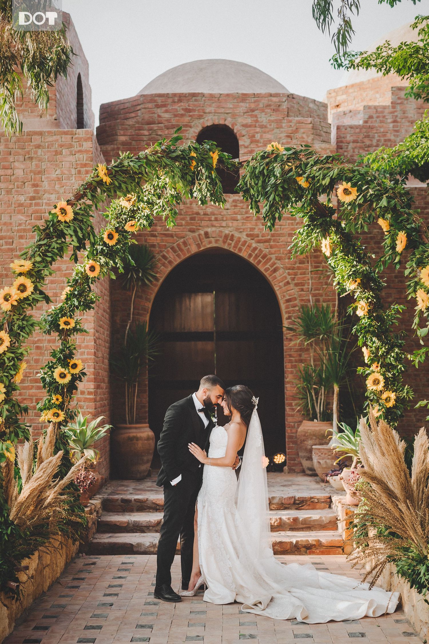 Wedding couple poses in front of rustic brick archways decorated with sunflowers.