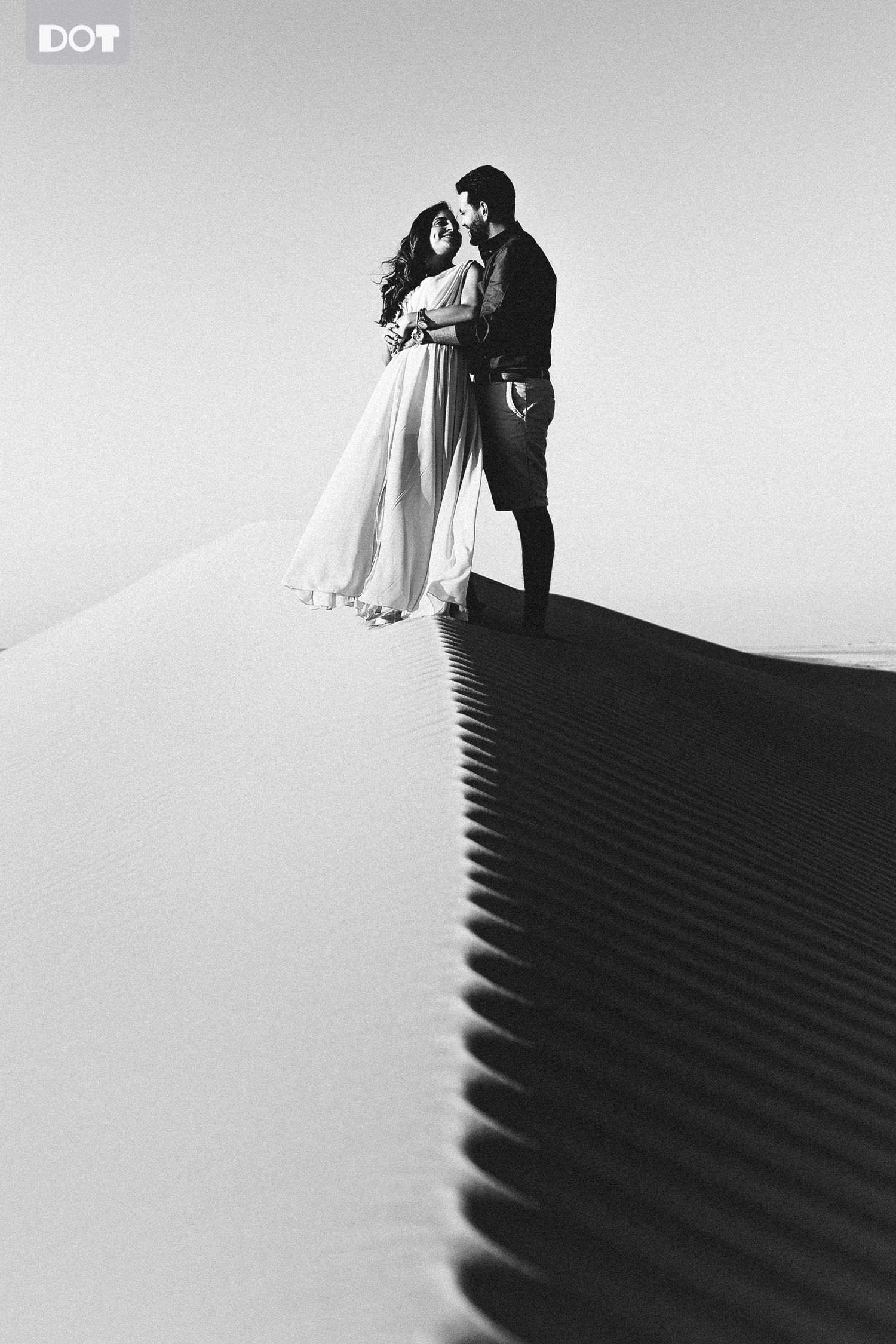 Artistic black and white photos of a couple on sand dunes creating dramatic shadows.