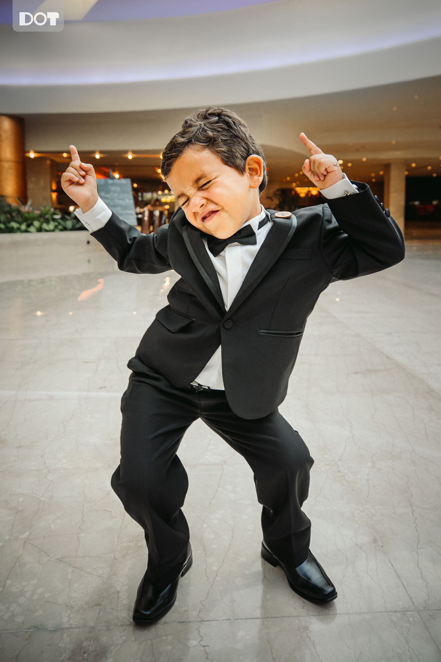 Young ring bearer in formal suit dances energetically on a polished floor.