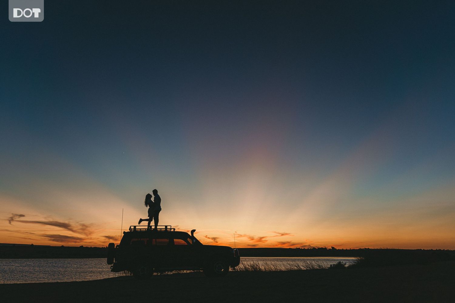 Silhouetted figures against vibrant sunset sky over ocean horizon.