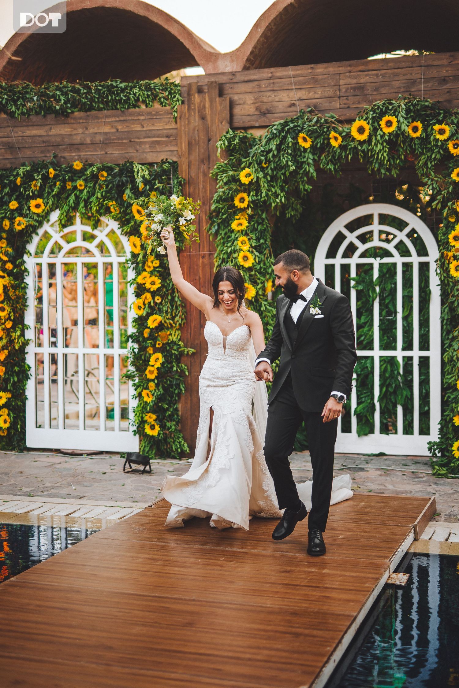 Wedding couple dances on wooden deck surrounded by sunflowers and white lattice arches.