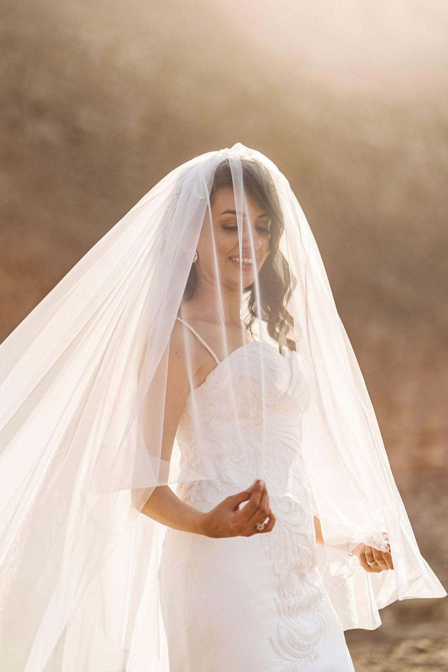 Ethereal bridal portrait with flowing white veil catching sunlight in golden hour.