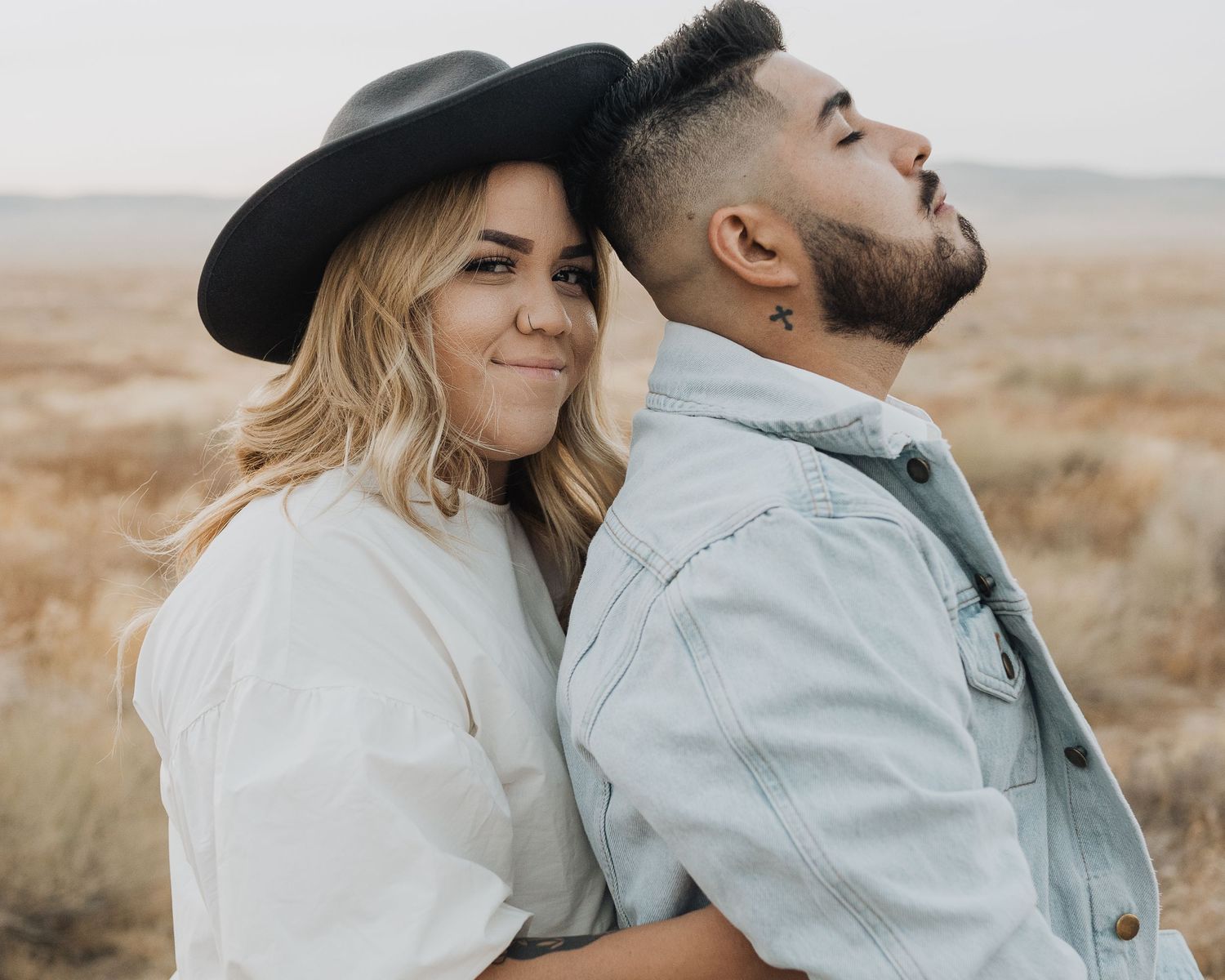 Romantic couple in casual attire embracing in a desert landscape during golden hour.