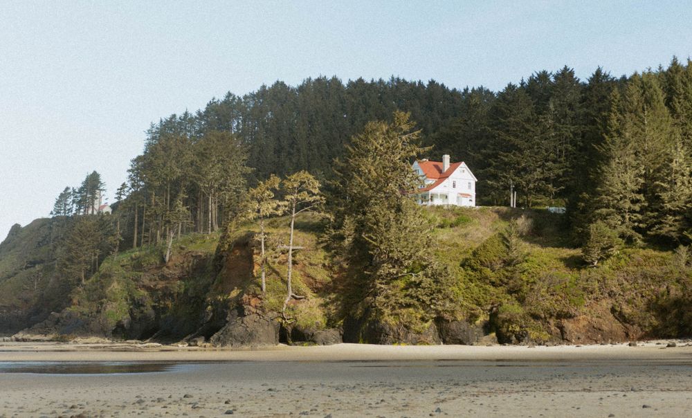 Coastal landscape featuring a white lighthouse perched on a forested cliff overlooking the ocean.