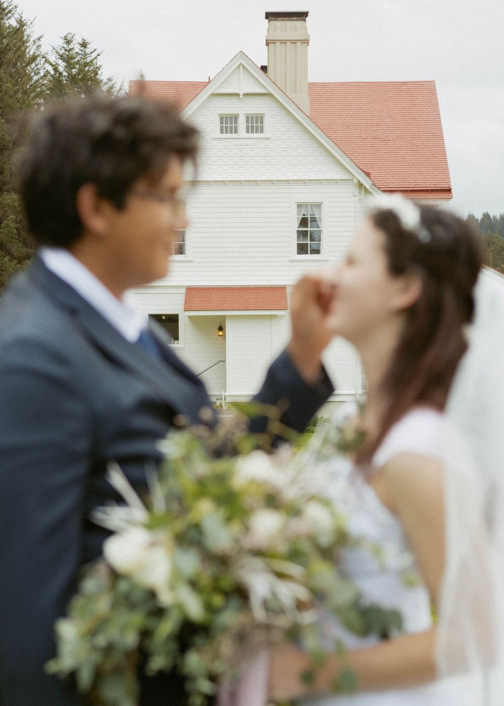 A wedding couple shares an intimate moment near white buildings with a bouquet.