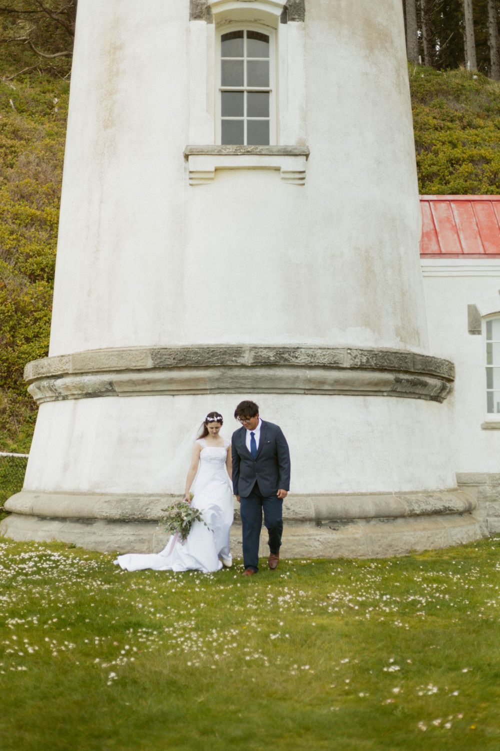 A couple sits together against a white lighthouse wall surrounded by wildflowers.