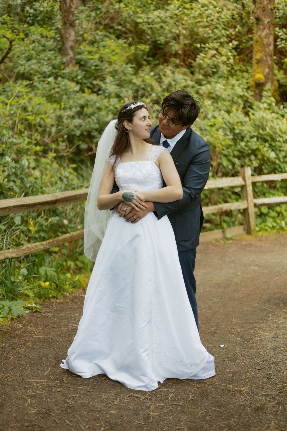 A romantic moment captured on a forest trail surrounded by green foliage.