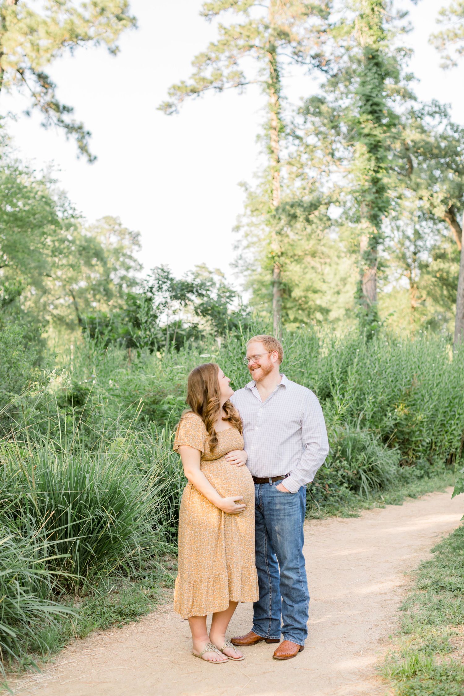 Expectant couple shares intimate moment on wooded trail during maternity photoshoot.