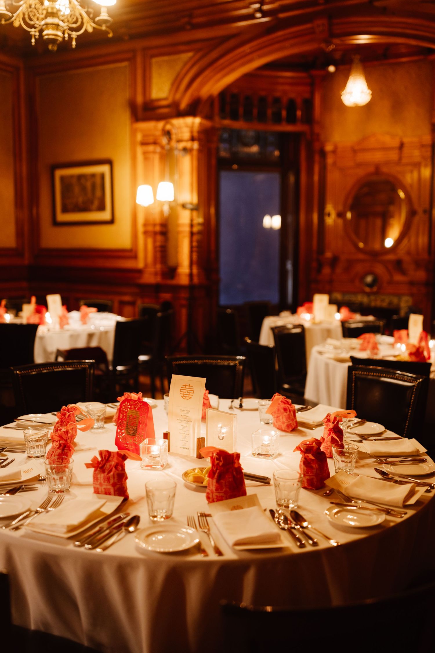 Round dining table elegantly set with red decor in a wood-paneled room with chandelier.
