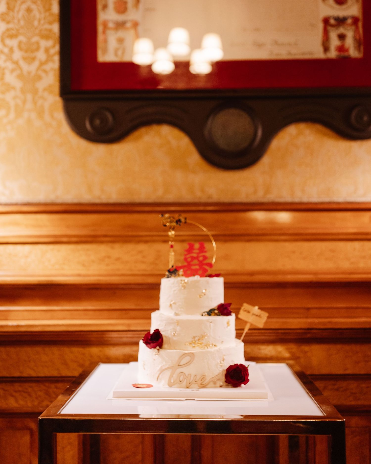 Three-tiered white wedding cake with red rose decorations on a wooden display stand.