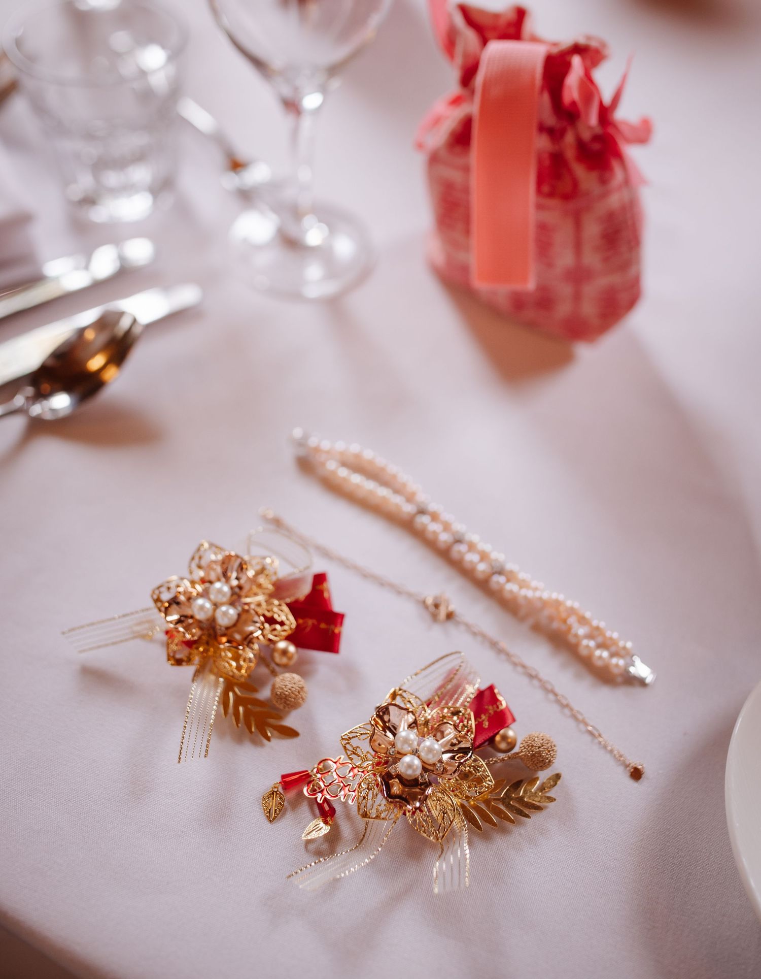 Gold and coral wedding accessories with pearls and floral details on a white tablecloth.