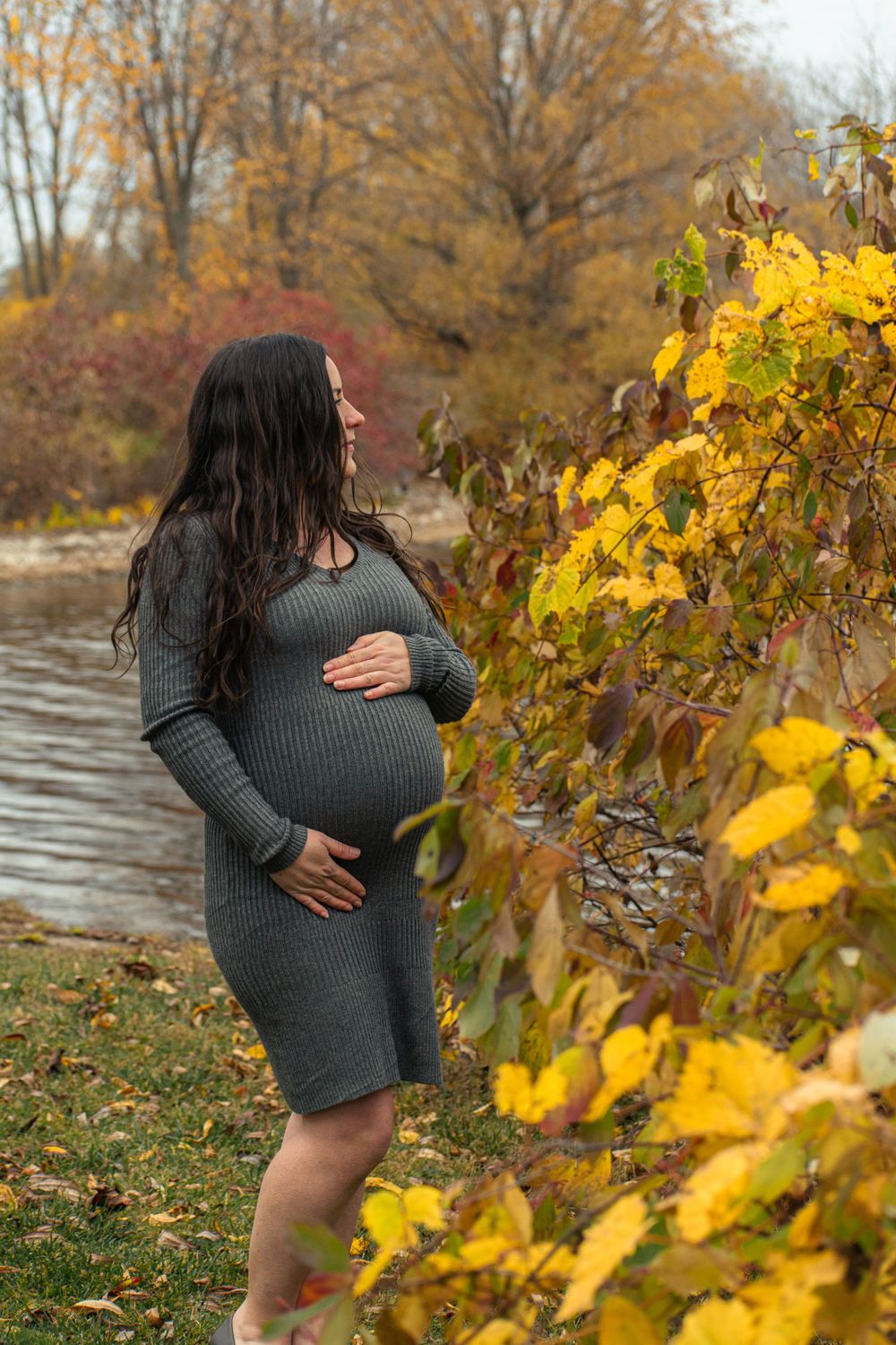 Maternity photo with bright yellow autumn leaves and lake in background.