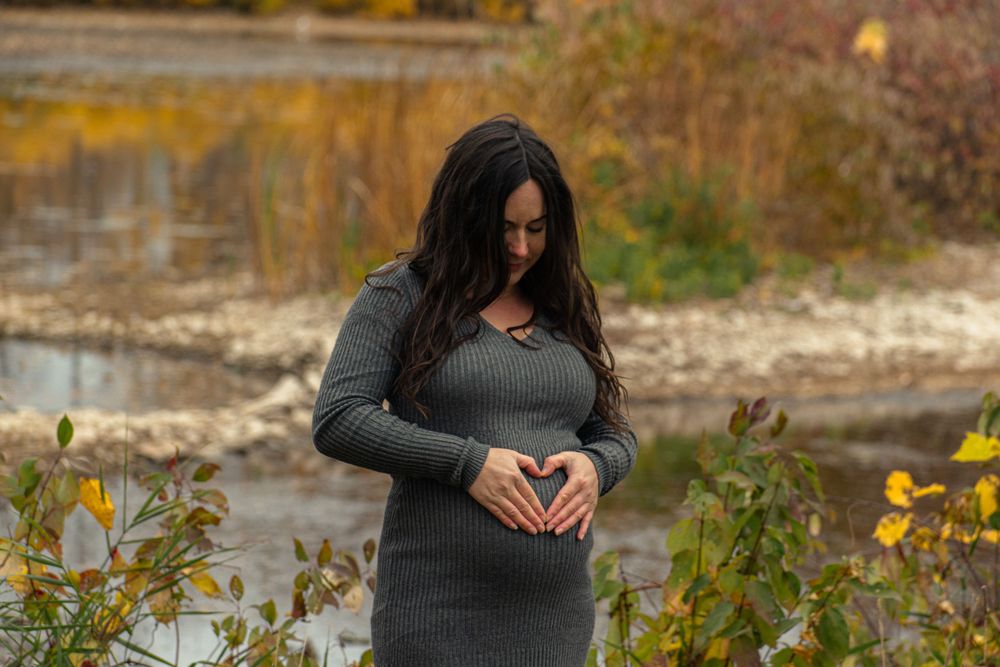Intimate maternity moment captured by lake with fall colors in background.