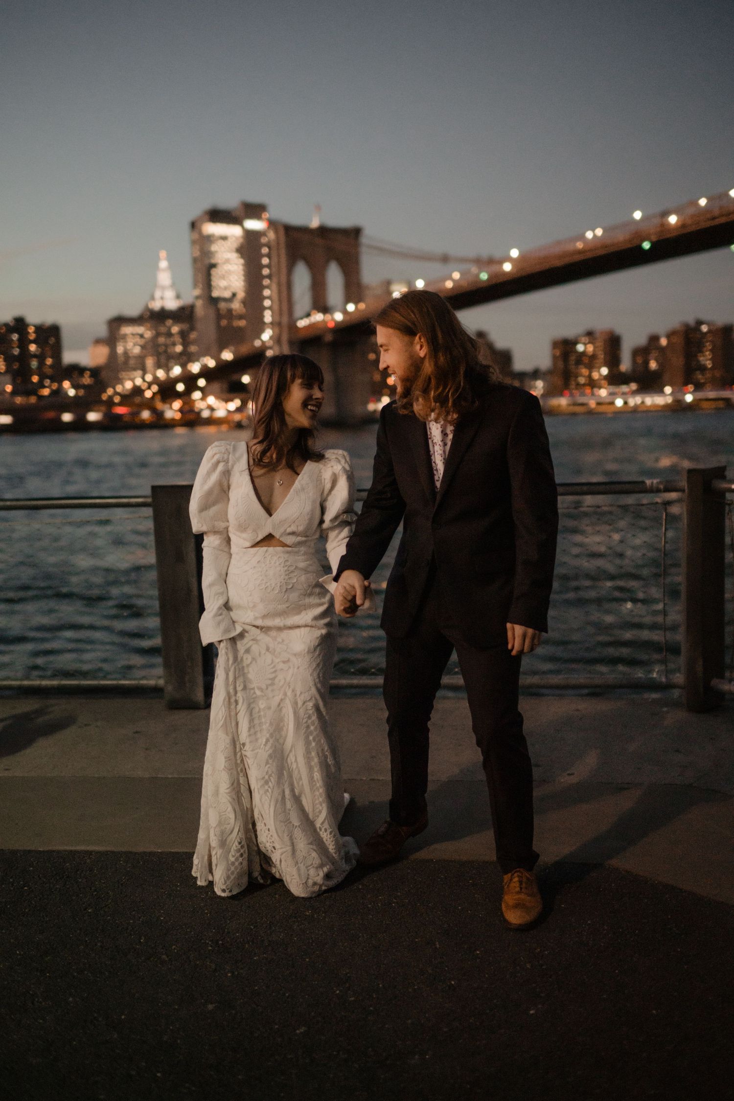 A romantic wedding photo with the Brooklyn Bridge and NYC skyline illuminated at dusk.